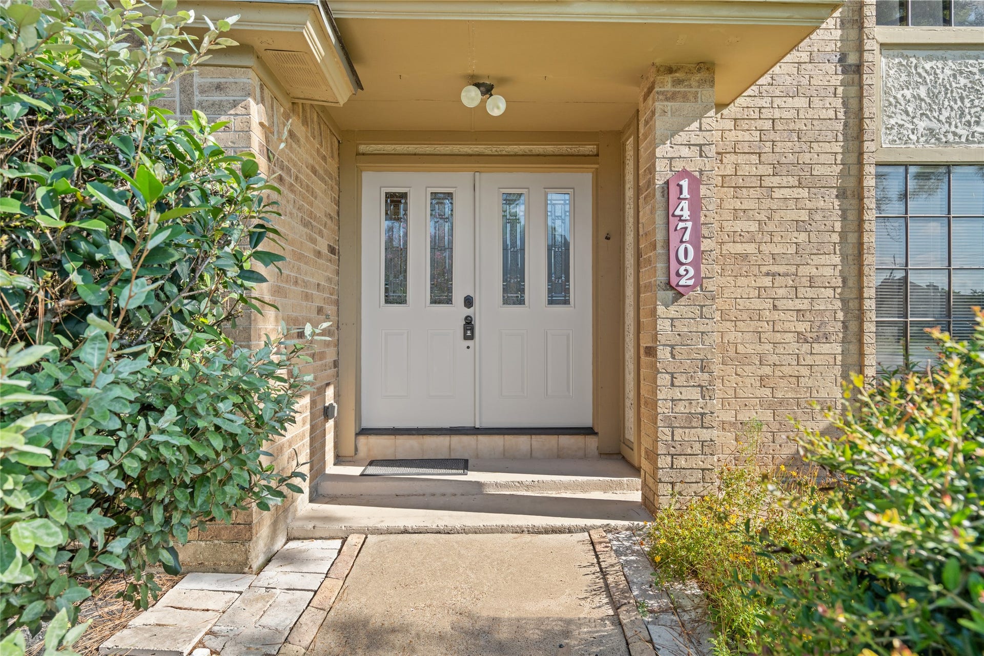 The double-door entrance framed by brick and lush landscaping creates an inviting transition from the outdoors into a home filled with character and possibilities.