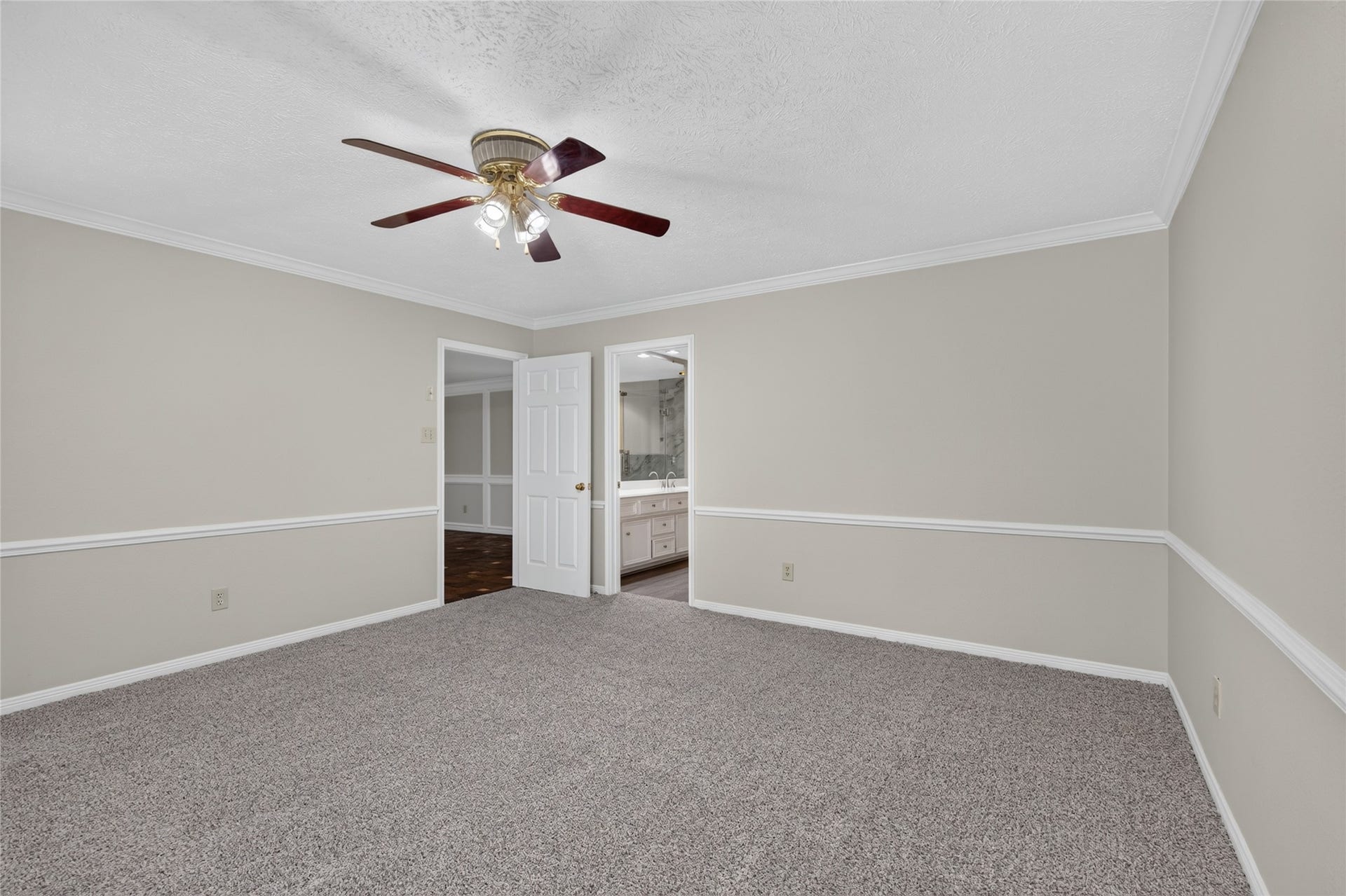 Plush carpeting, crown molding, and a ceiling fan create a comfortable bedroom environment with a convenient connection to the en-suite bath.