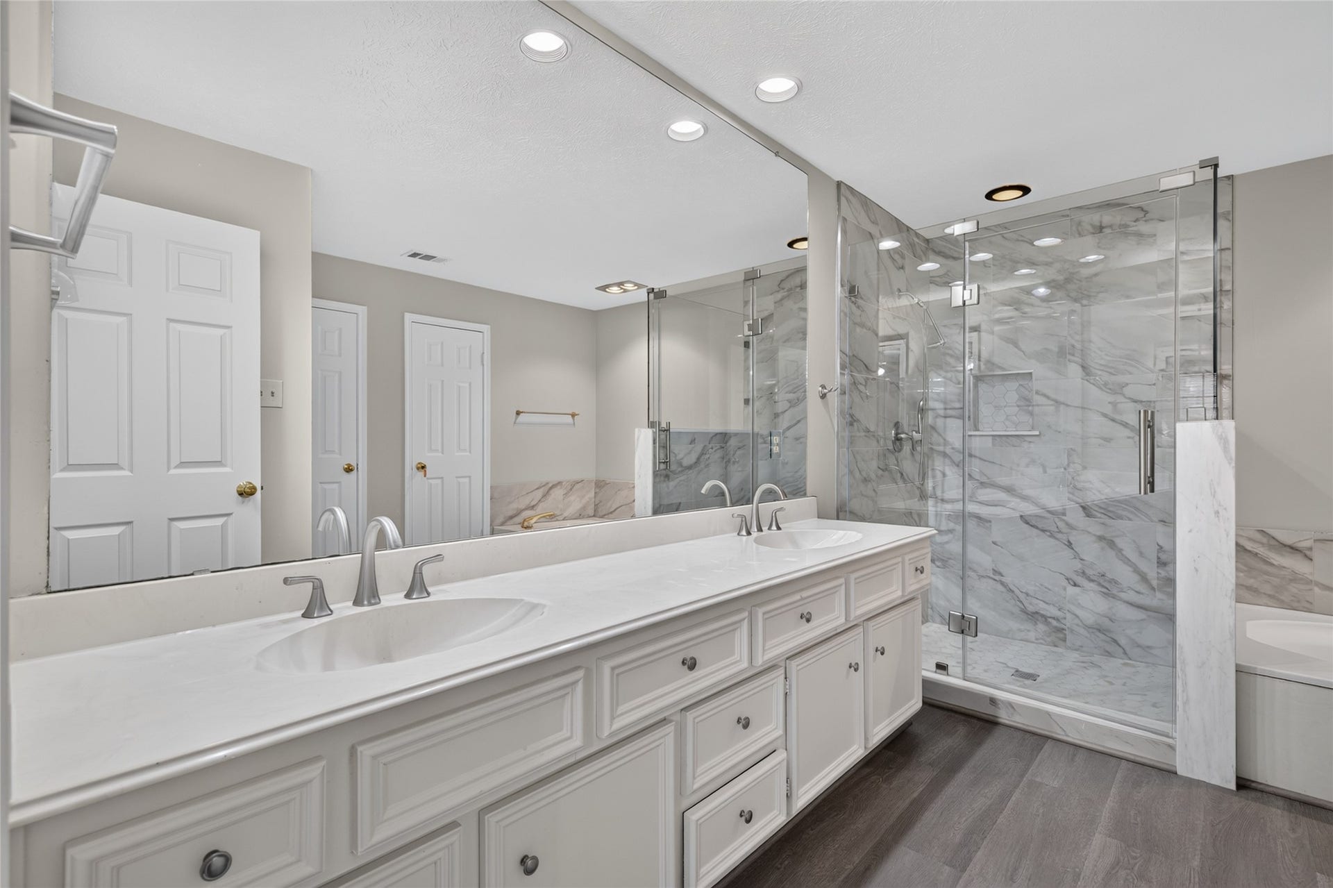 A spacious double vanity, marble countertops, and a glass-enclosed shower create a polished bathroom setting with the feel of a private retreat.