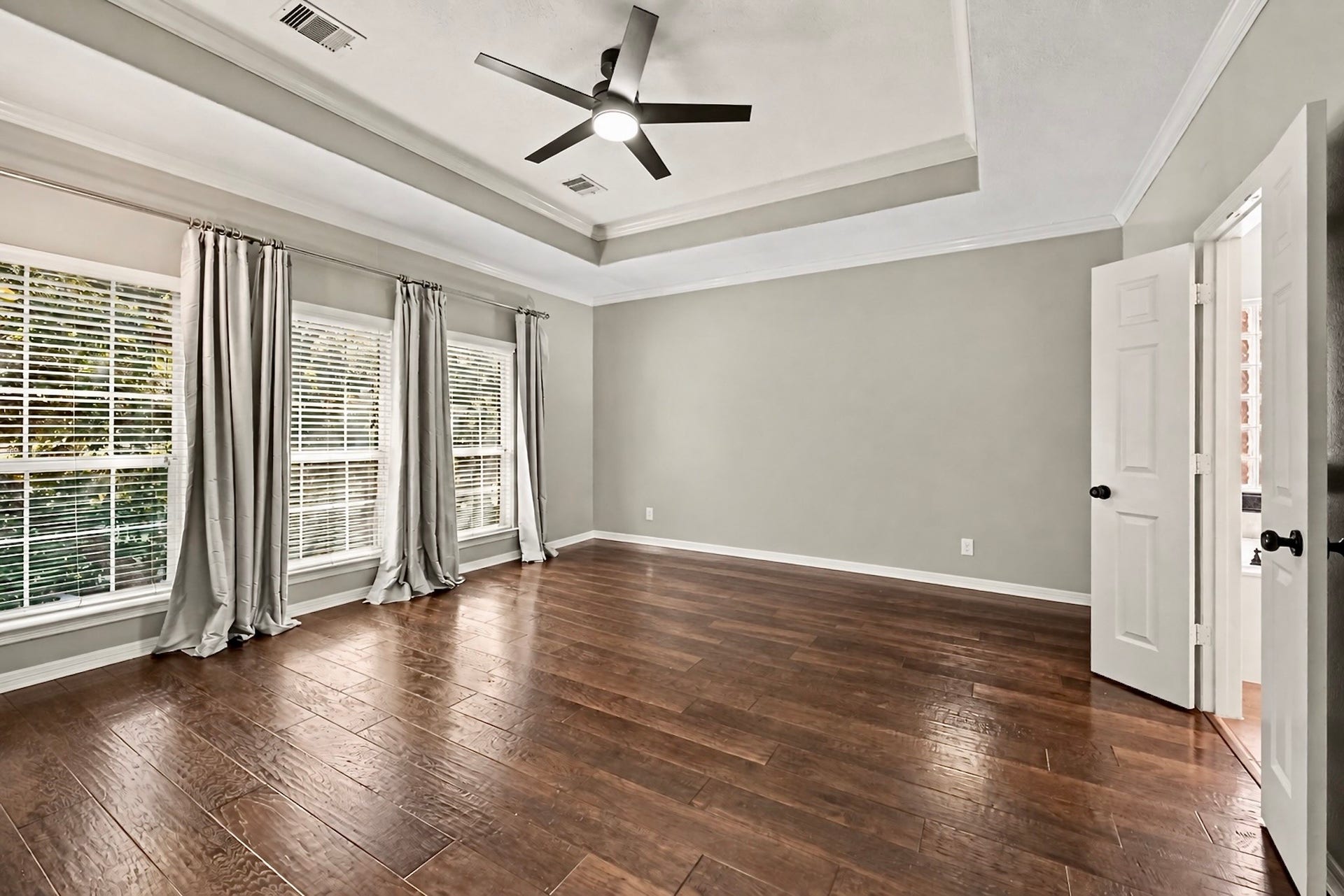 Expansive bedroom with tray ceiling, wood flooring, and a wall of windows.Virtually unstaged to highlight the rooms size and versatility.