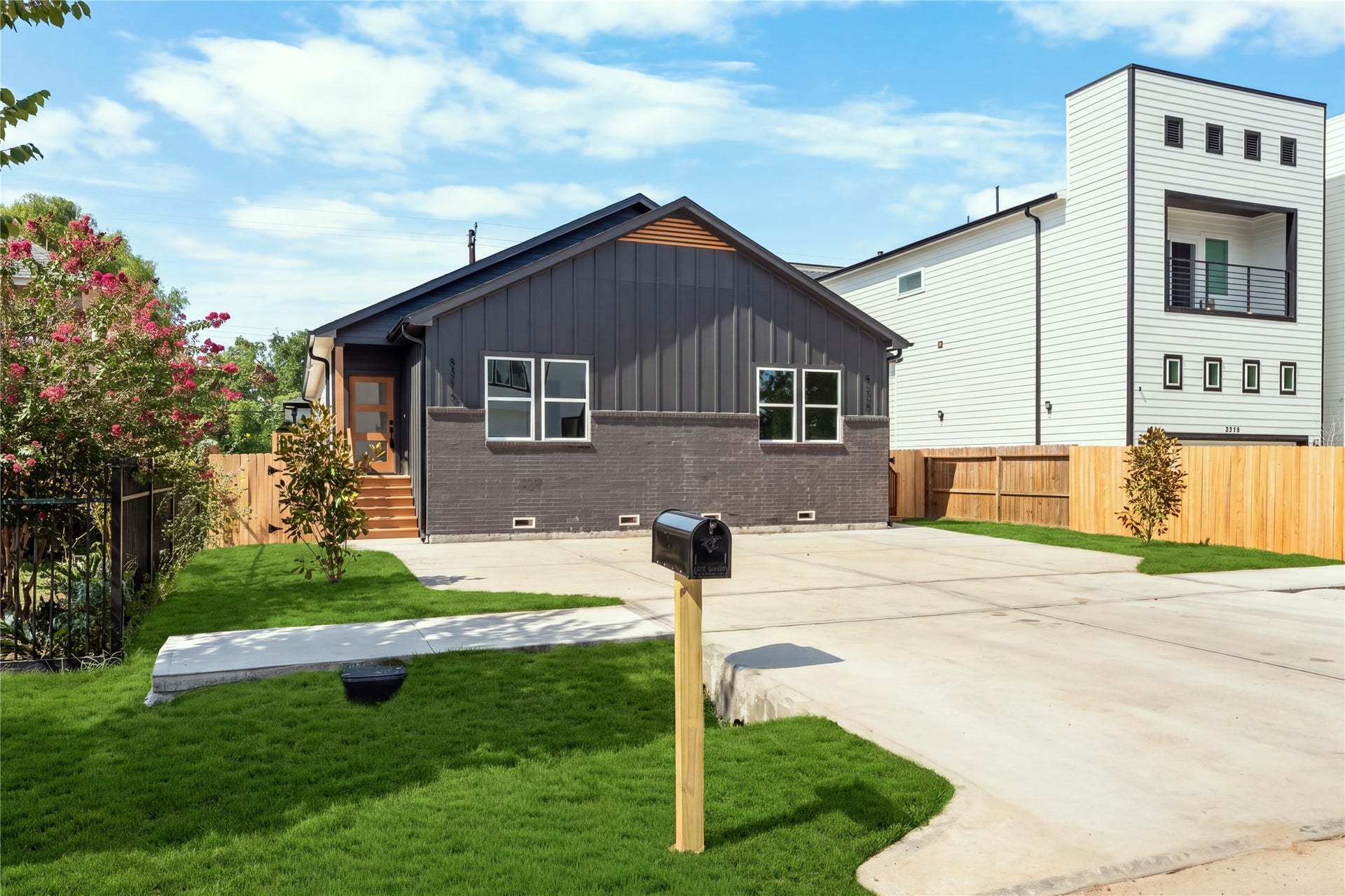 5321 Rue Street, Houston, TX 77033 Modern elevation with bold charcoal board-and-batten siding deep brick accents, double-entry wood steps, and an expansive concrete drive with ample parking space.