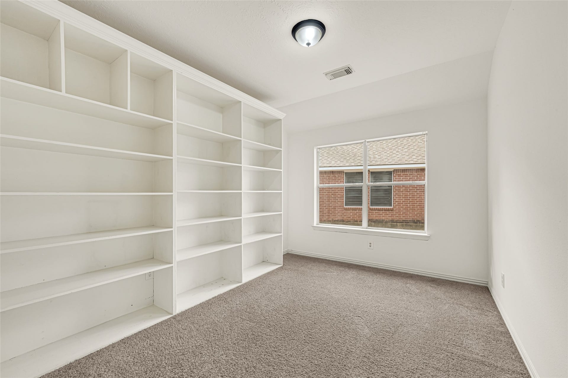 7102 Hollow Field Lane, Cypress, TX 77433 Versatile bedroom or study showcasing an entire wall of custom built-in shelving, making it the perfect setup for a home library or organized workspace.