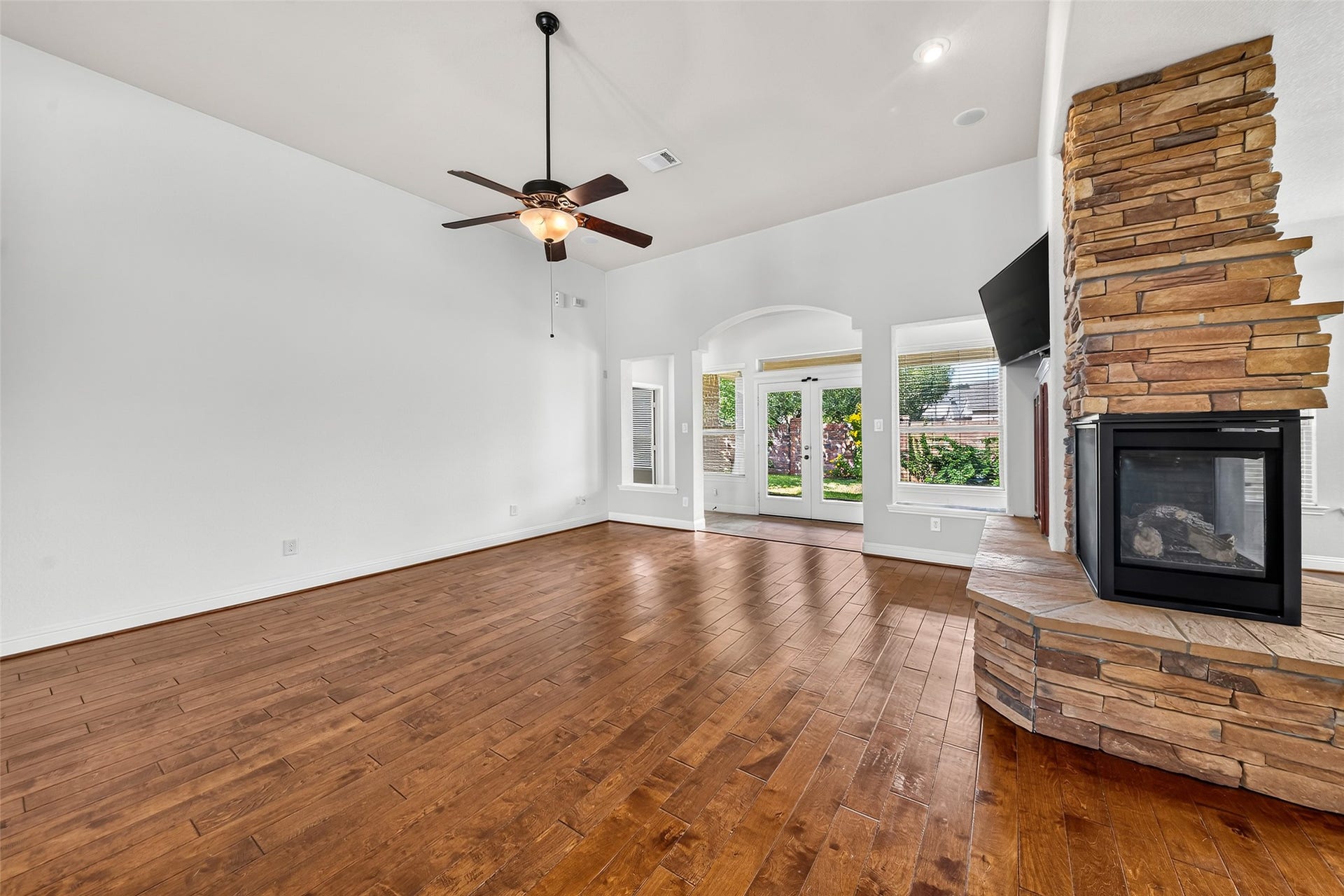 12218 Rampy Green Drive, Tomball, TX 77377 Expansive living room featuring high, elegant ceilings, stunning wooden floors, a charming stone fireplace, ample natural light, and French doors that lead to the backyard.