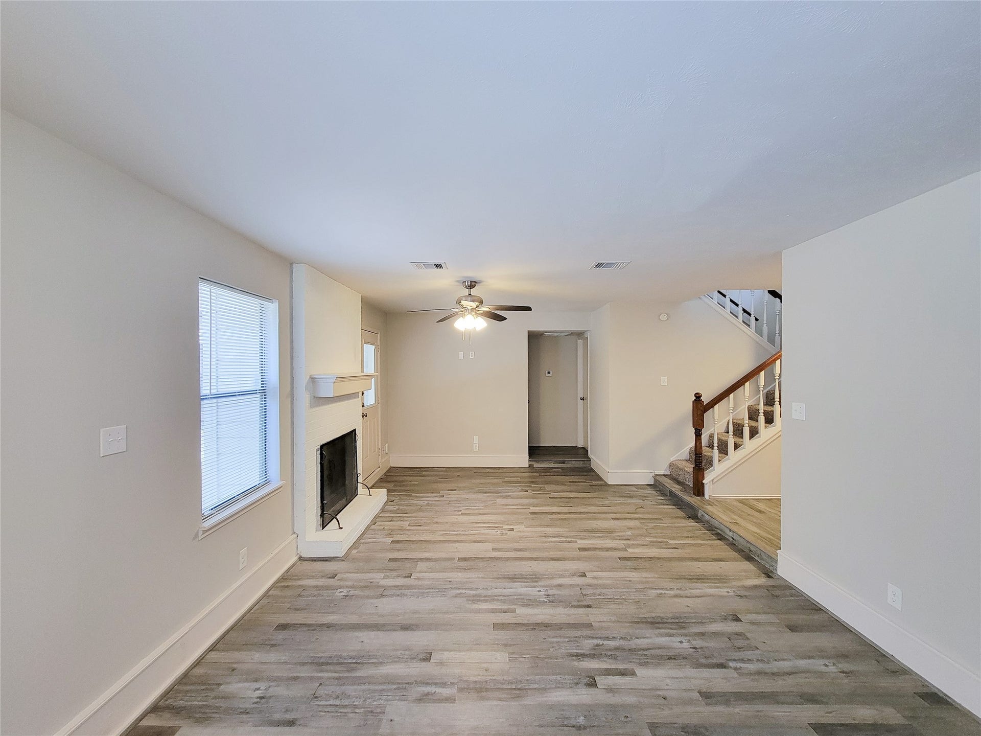 80 Fallenstone Drive, The Woodlands, TX 77381 Spacious living area with stylish wood flooring, a cozy fireplace, and a ceiling fan, complemented by natural light from large windows.