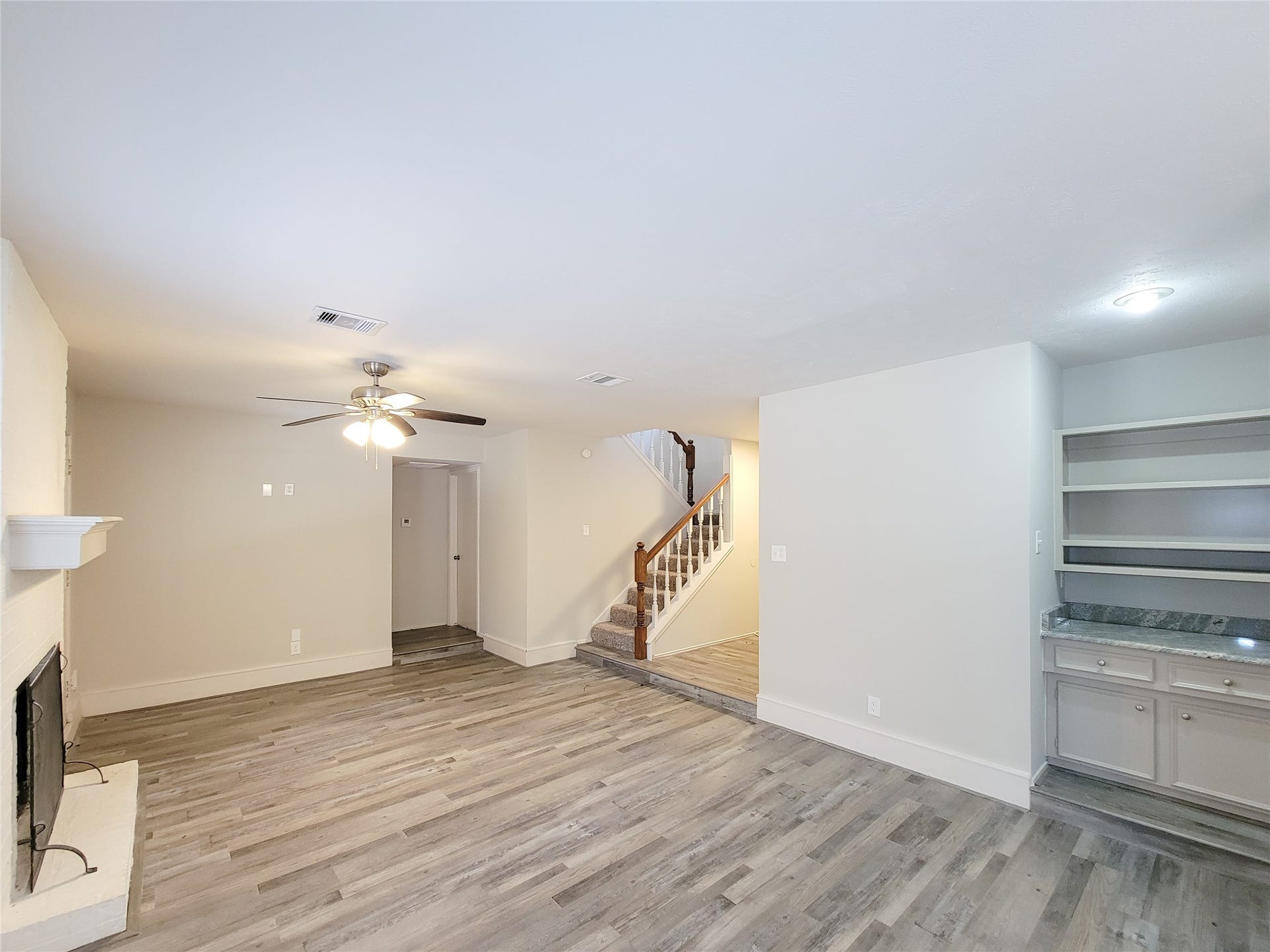 80 Fallenstone Drive, The Woodlands, TX 77381 Spacious living area with modern wood-look flooring, a cozy fireplace, built-in shelving, and a ceiling fan, leading to an inviting staircase.