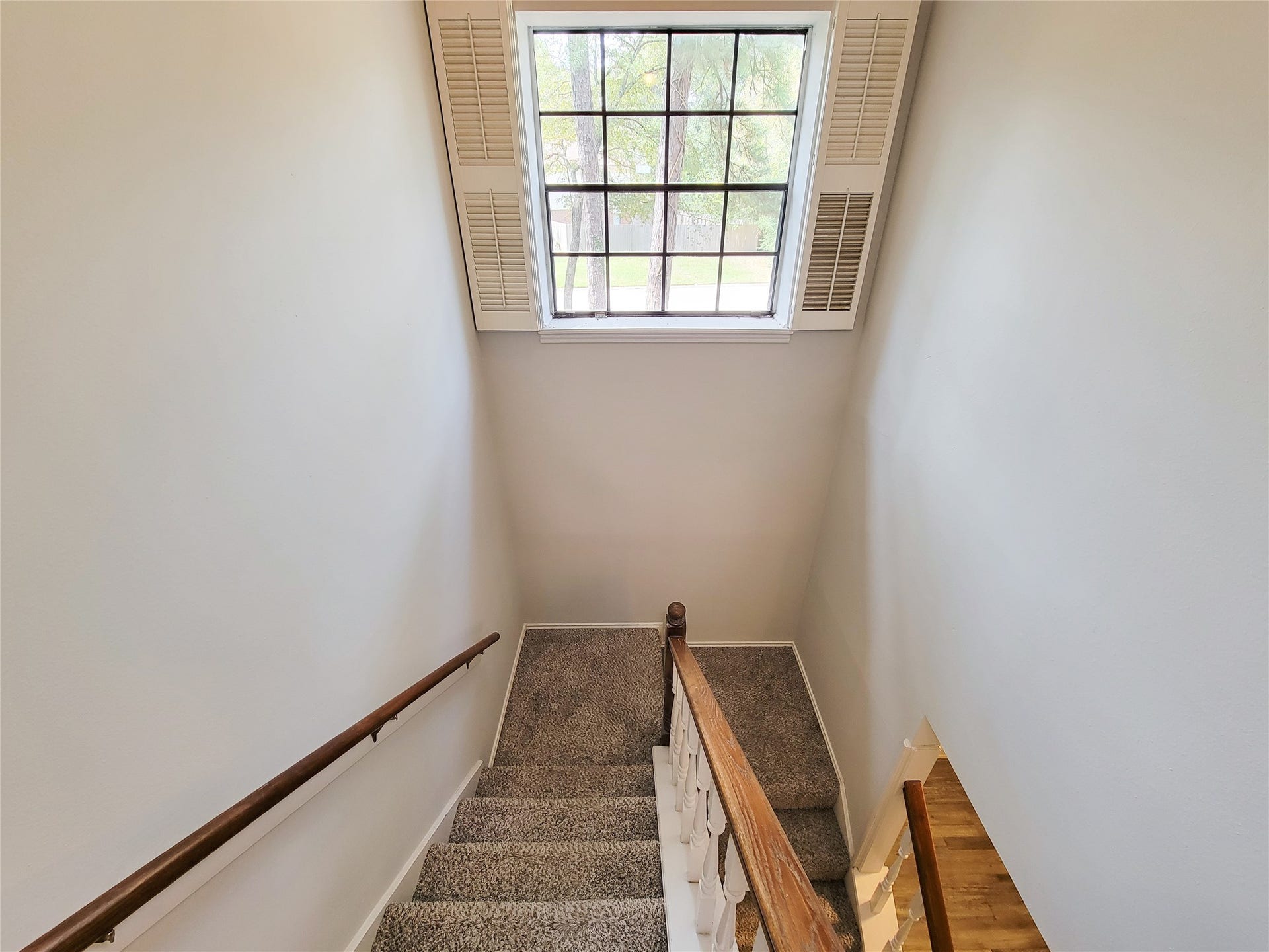 80 Fallenstone Drive, The Woodlands, TX 77381 Bright and inviting staircase with a large window letting in natural light, featuring neutral walls and carpeted steps for a cozy ascent.