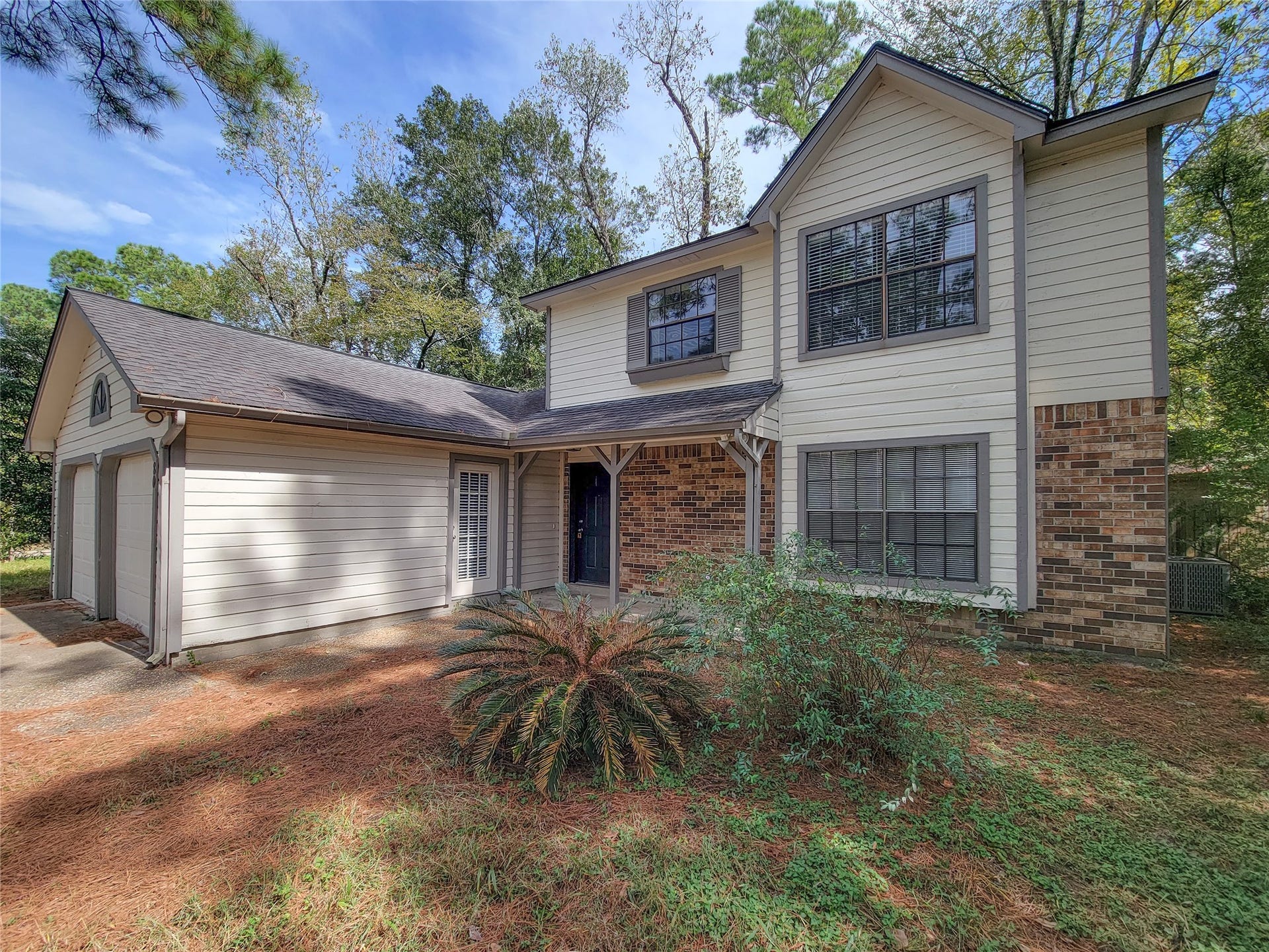 80 Fallenstone Drive, The Woodlands, TX 77381 Charming two-story home with a mix of brick and siding, featuring a spacious attached garage and surrounded by lush greenery for added privacy.