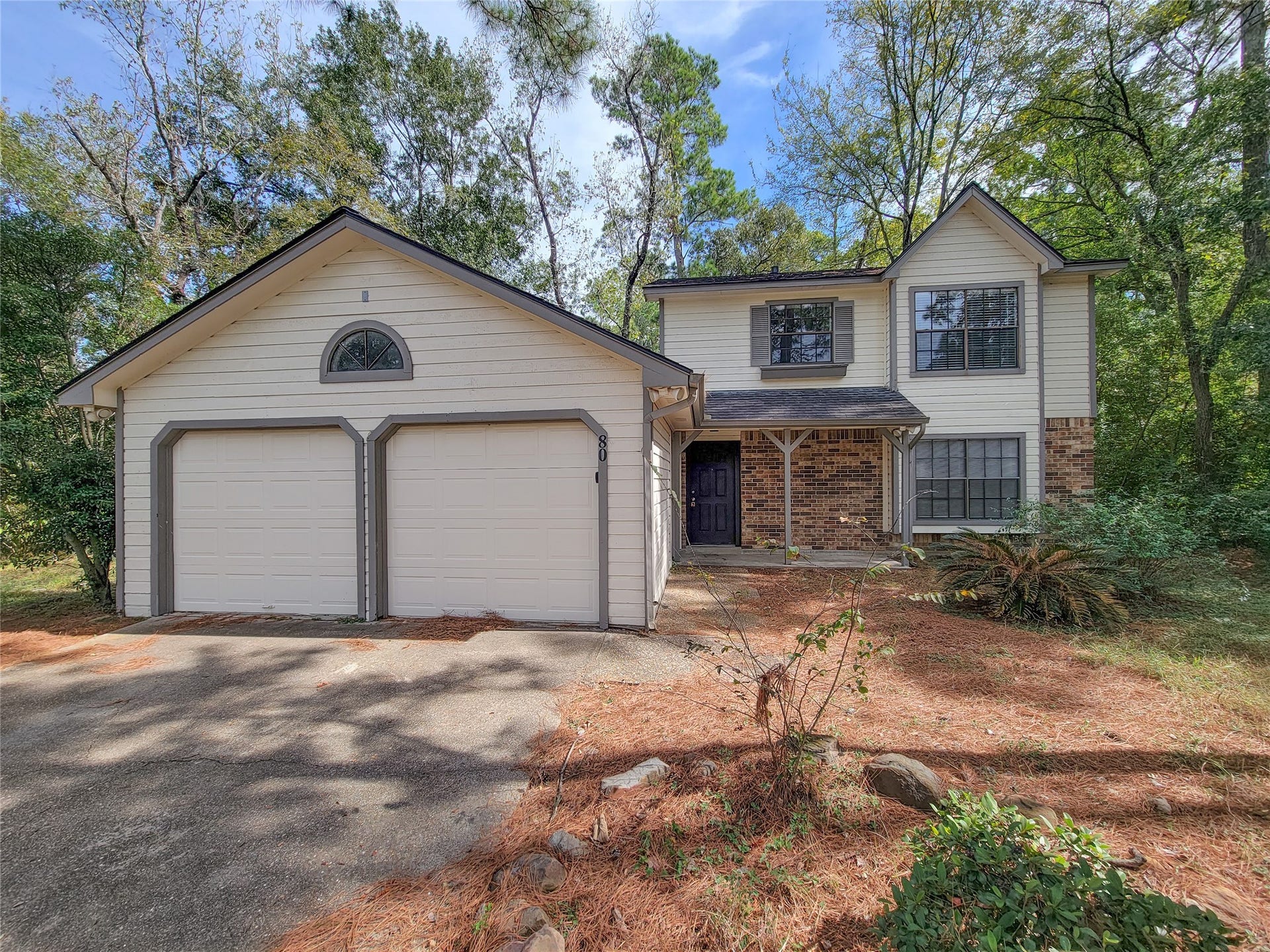 80 Fallenstone Drive, The Woodlands, TX 77381 Charming two-story home with a spacious two-car garage, surrounded by lush greenery and nestled in a serene wooded setting.