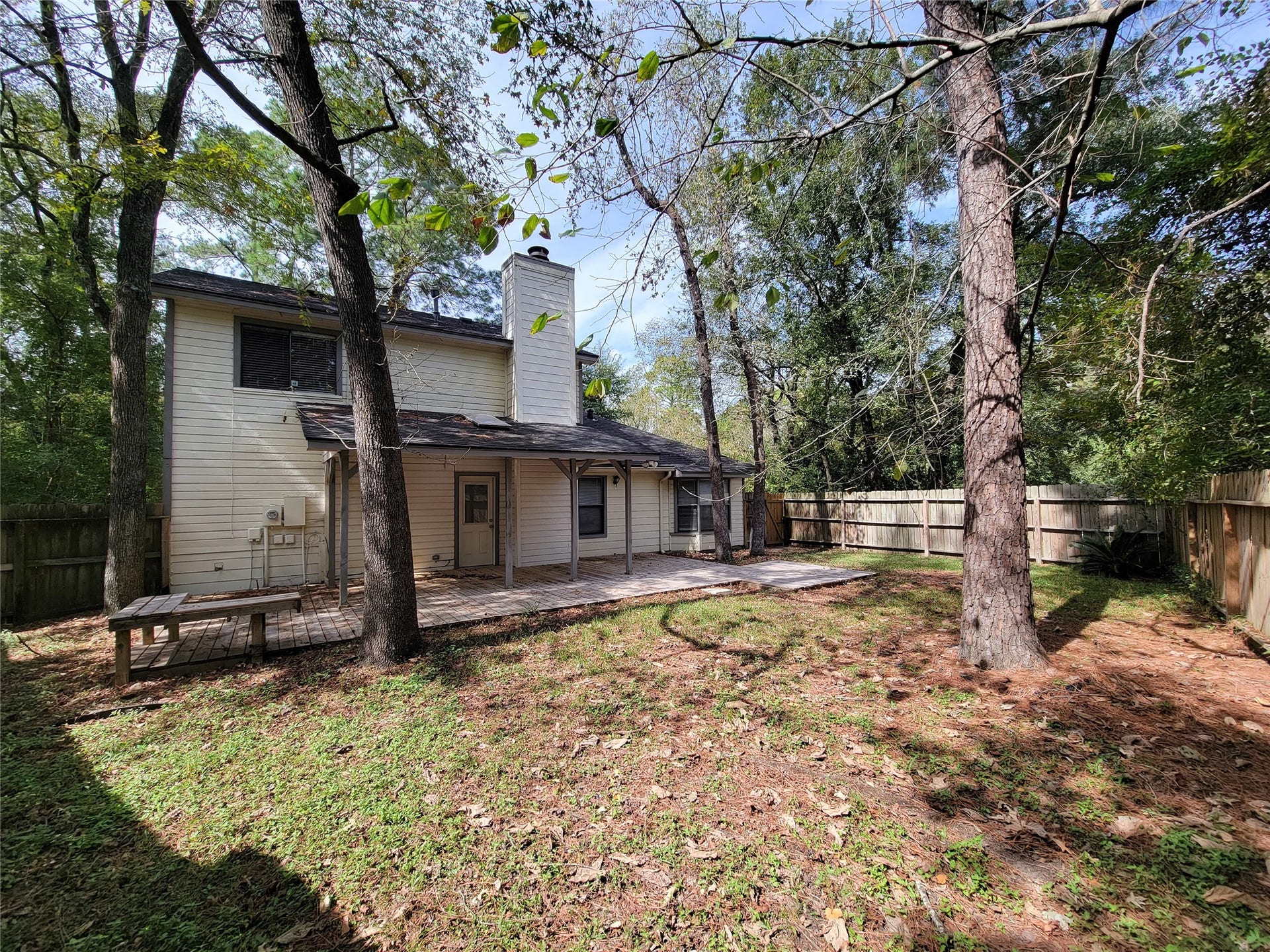 80 Fallenstone Drive, The Woodlands, TX 77381 Spacious backyard with mature trees and a charming two-story home, featuring a cozy patio area perfect for outdoor gatherings.