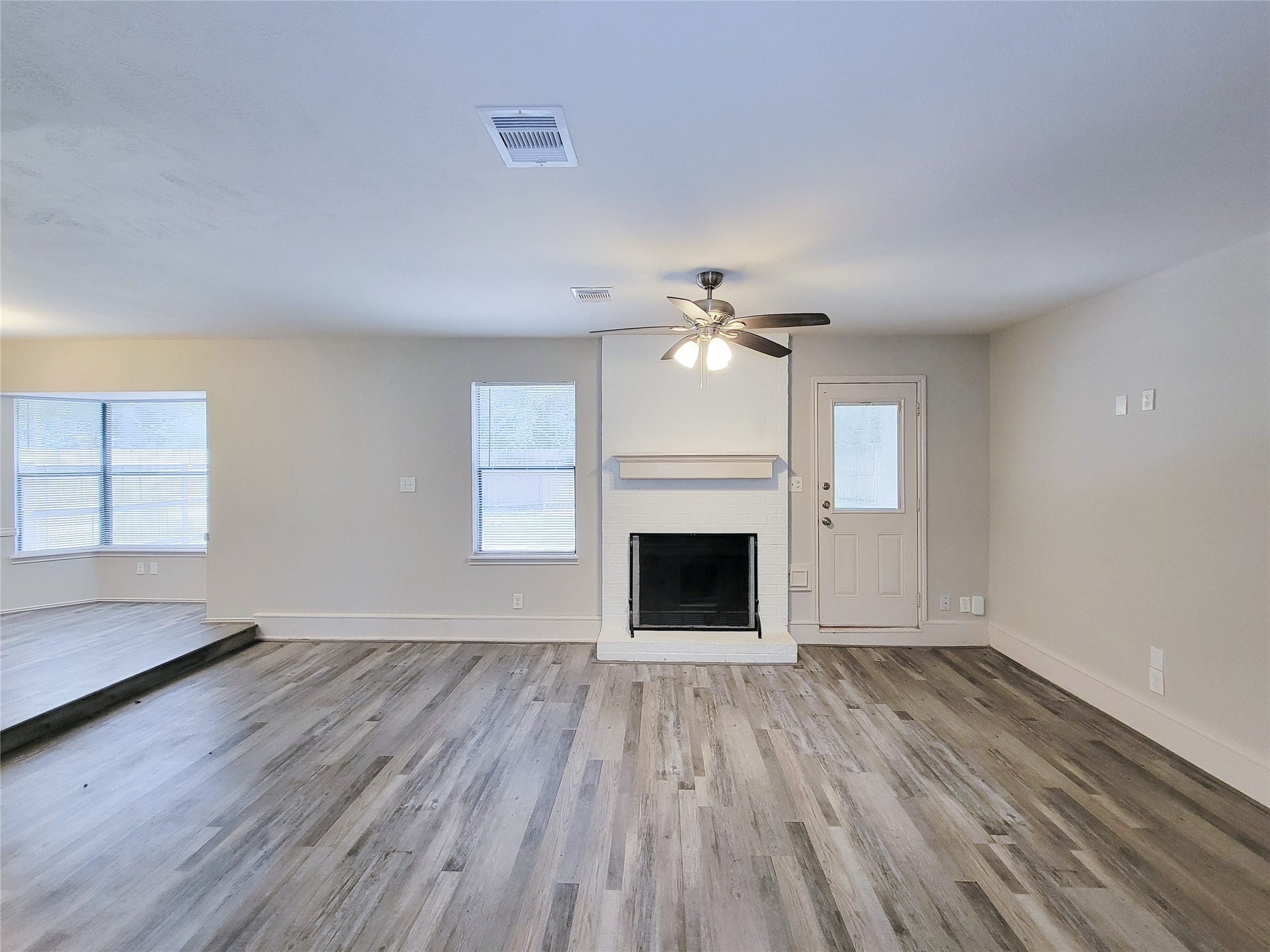 80 Fallenstone Drive, The Woodlands, TX 77381 Spacious living room with elegant wood flooring, a cozy fireplace, ceiling fan, and ample natural light through large windows.