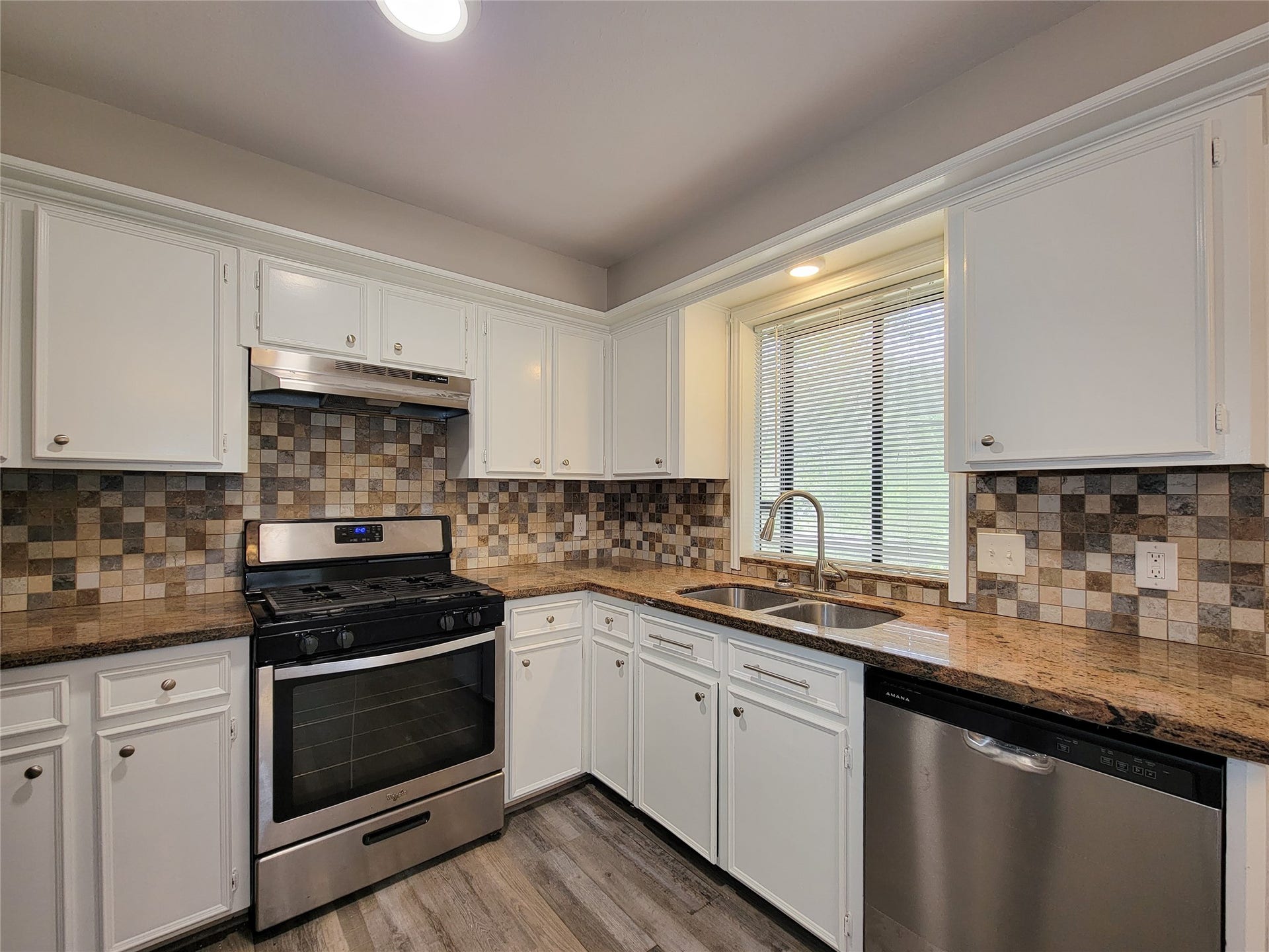 80 Fallenstone Drive, The Woodlands, TX 77381 Modern kitchen with stainless steel appliances, elegant granite countertops, and a stylish tiled backsplash, complemented by ample white cabinetry and a double sink.
