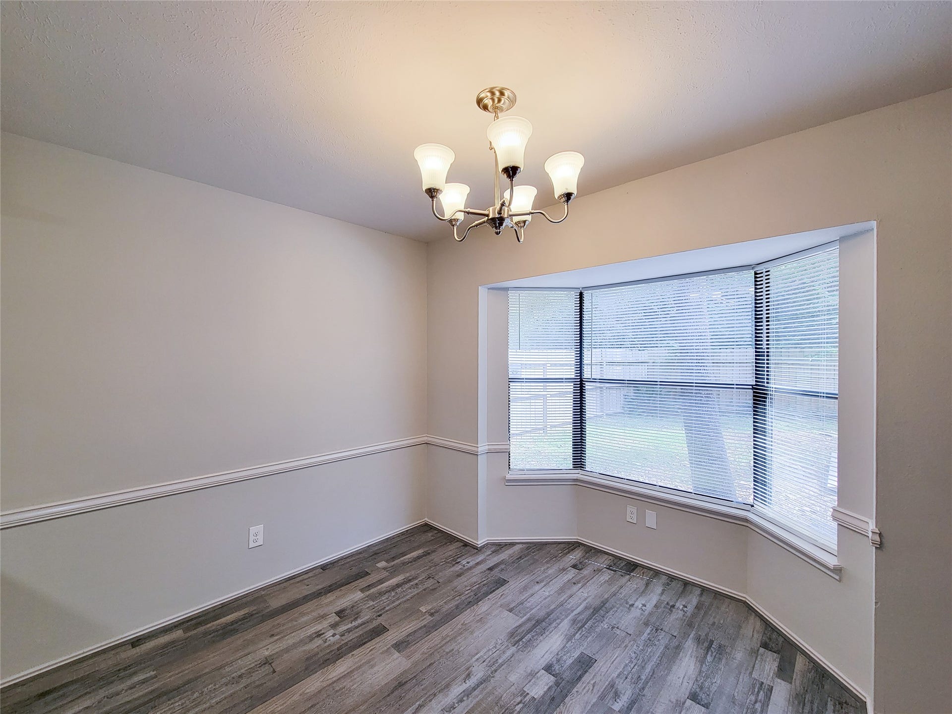 80 Fallenstone Drive, The Woodlands, TX 77381 Bright dining area featuring a stylish chandelier, elegant wainscoting, and a large bay window offering natural light and views of the backyard.