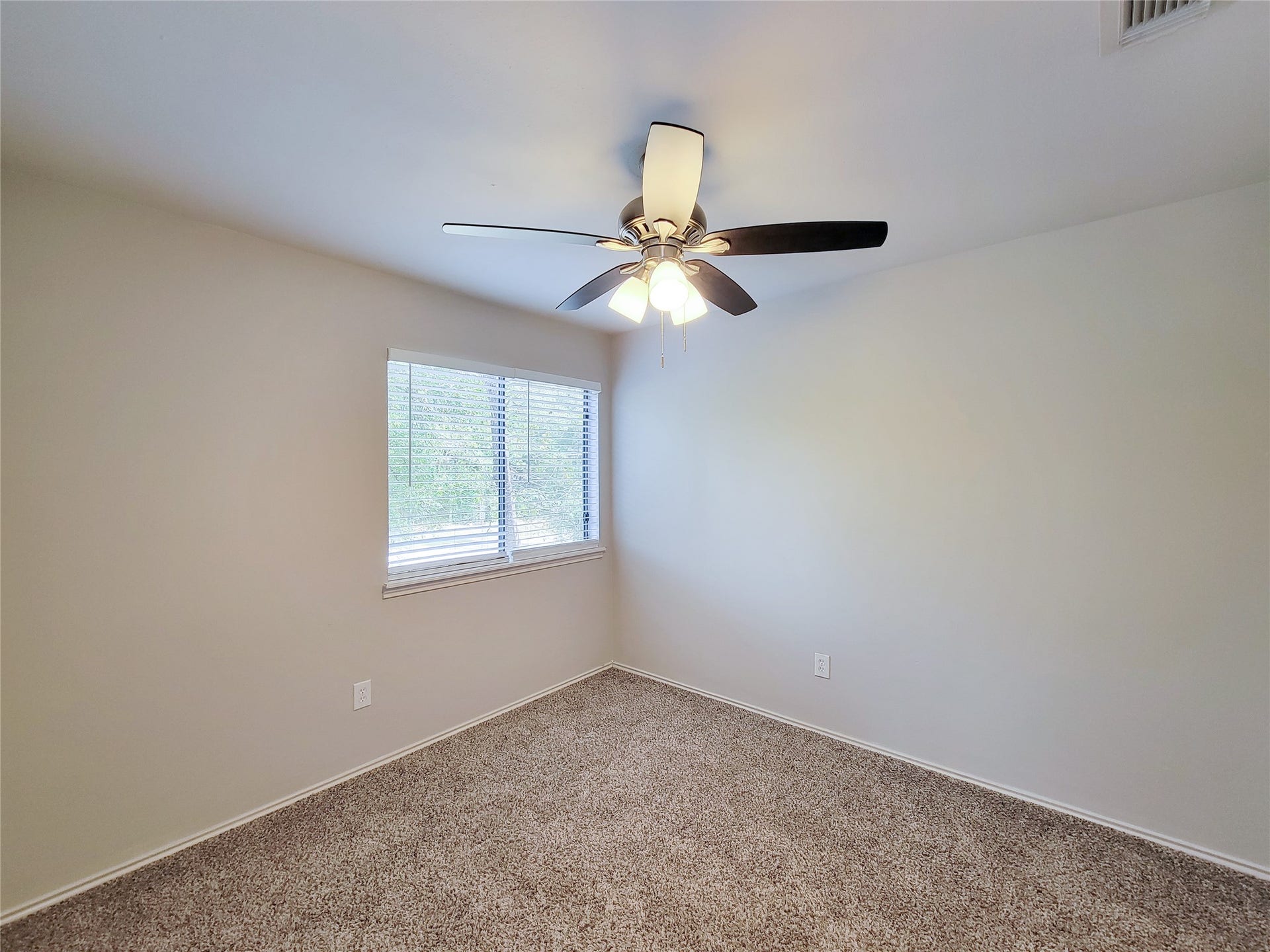 80 Fallenstone Drive, The Woodlands, TX 77381 Cozy bedroom with plush carpeting, featuring a ceiling fan and natural light streaming through a large window.