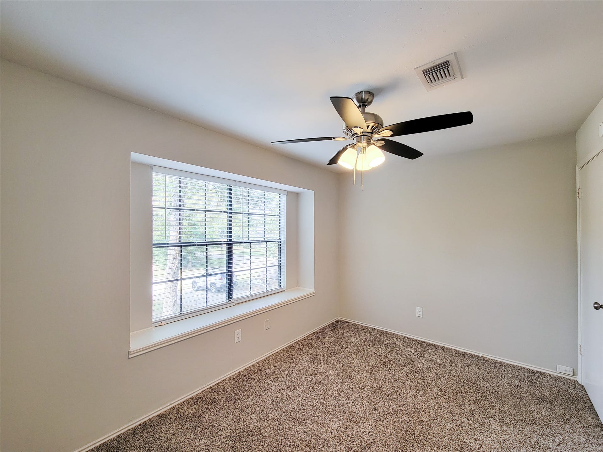 80 Fallenstone Drive, The Woodlands, TX 77381 Bright and cozy room featuring a large window with views of greenery, neutral walls, plush carpet, and a stylish ceiling fan.