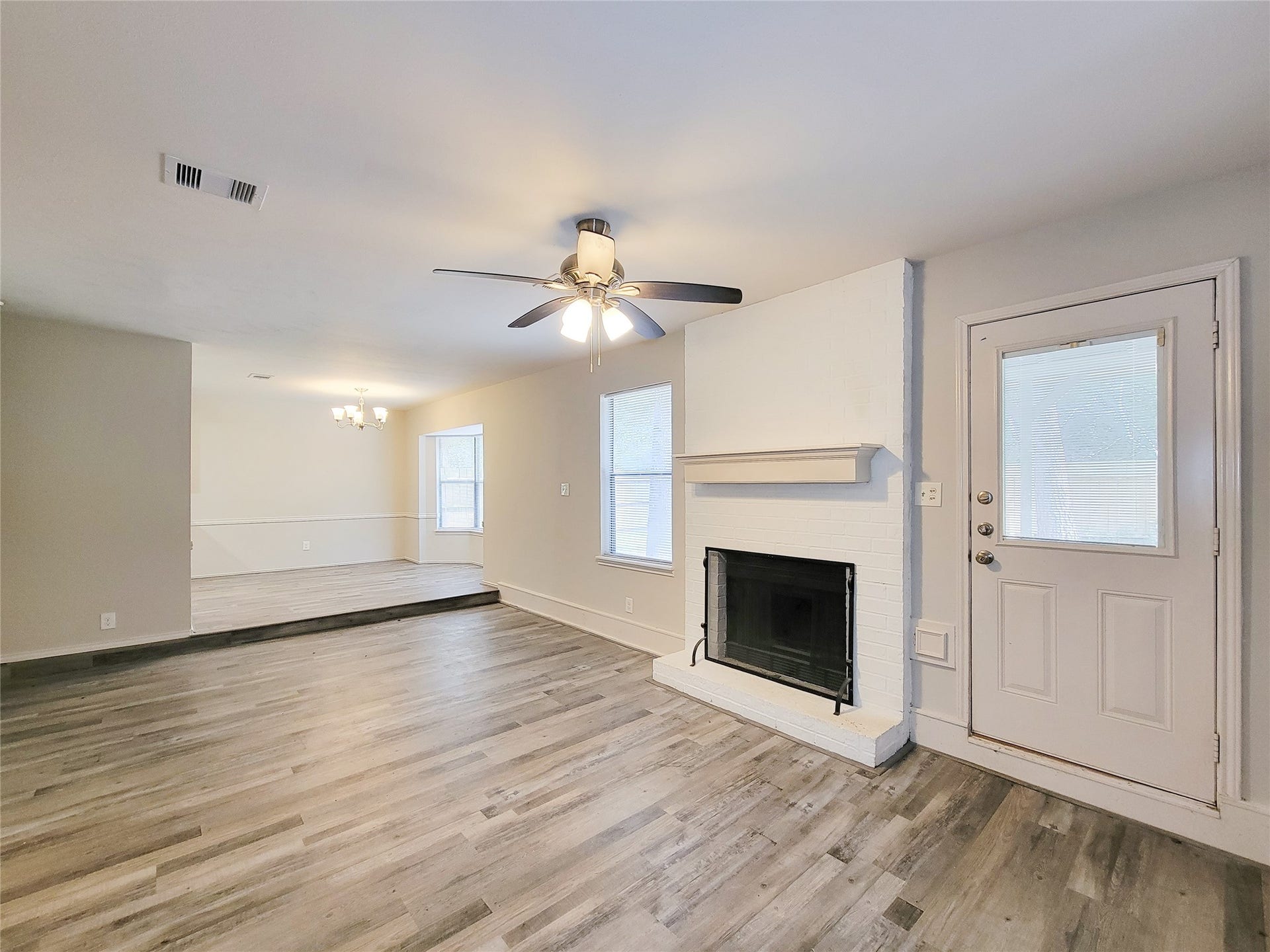 80 Fallenstone Drive, The Woodlands, TX 77381 Spacious living area featuring laminate wood flooring, a cozy white brick fireplace, and abundant natural light, seamlessly flowing into an elevated dining space.