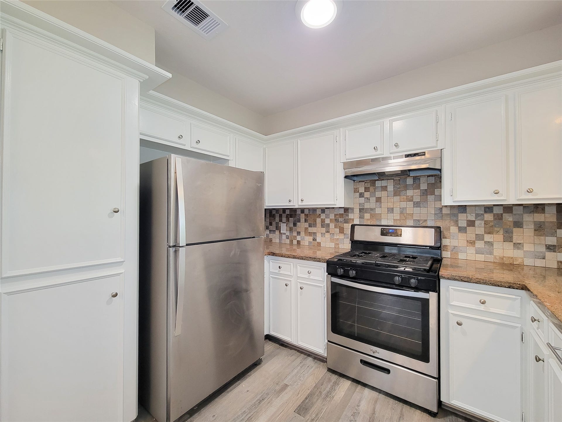80 Fallenstone Drive, The Woodlands, TX 77381 Charming kitchen with stainless steel appliances, ample white cabinetry, and a stylish mosaic tile backsplash.