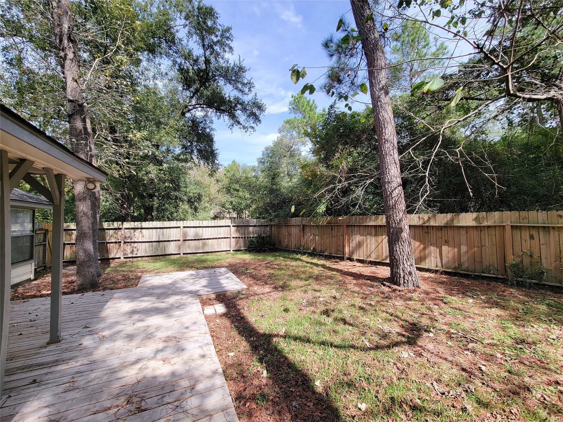 80 Fallenstone Drive, The Woodlands, TX 77381 Spacious backyard with a wooden deck, surrounded by lush greenery and a privacy fence, perfect for outdoor relaxation.