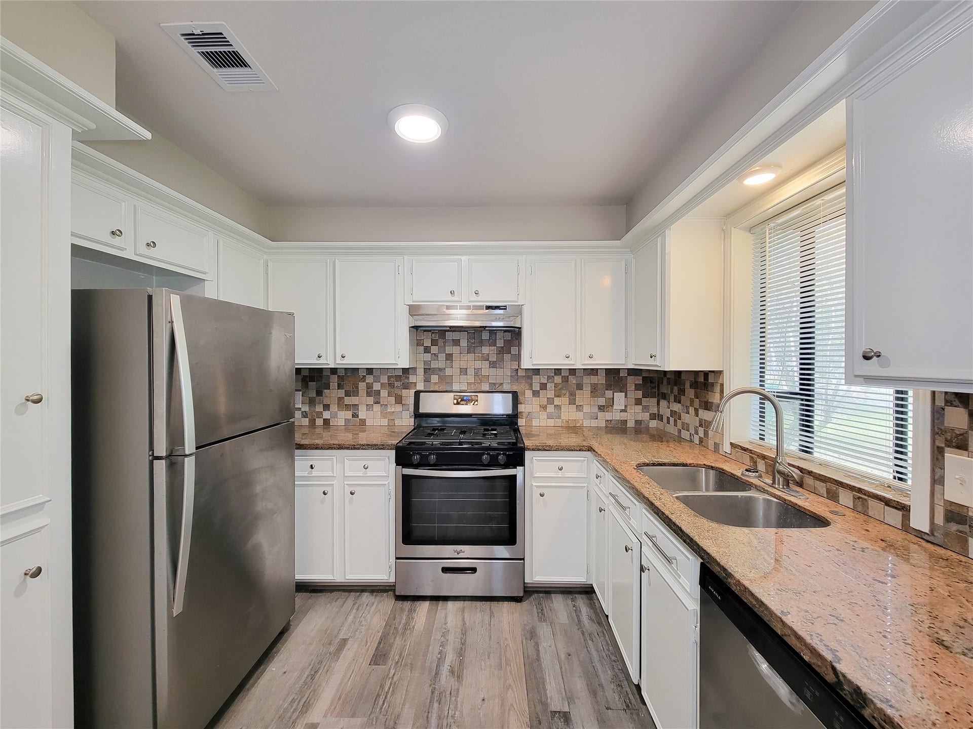 80 Fallenstone Drive, The Woodlands, TX 77381 Charming kitchen with sleek stainless steel appliances, elegant granite countertops, and a stylish tile backsplash, enhanced by ample cabinet space and natural light from the window.