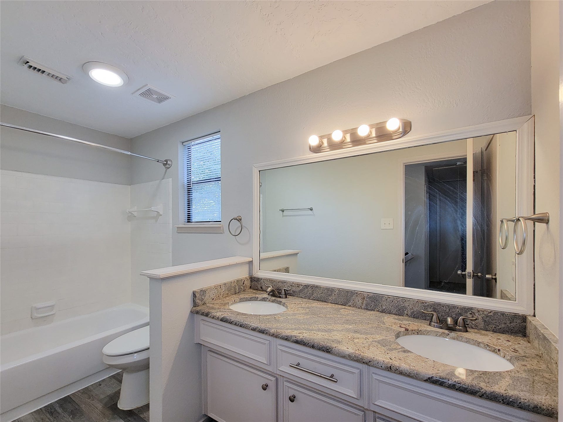 80 Fallenstone Drive, The Woodlands, TX 77381 Bright and modern bathroom featuring a double vanity with elegant granite countertops, a spacious mirror, and a classic shower-tub combination.