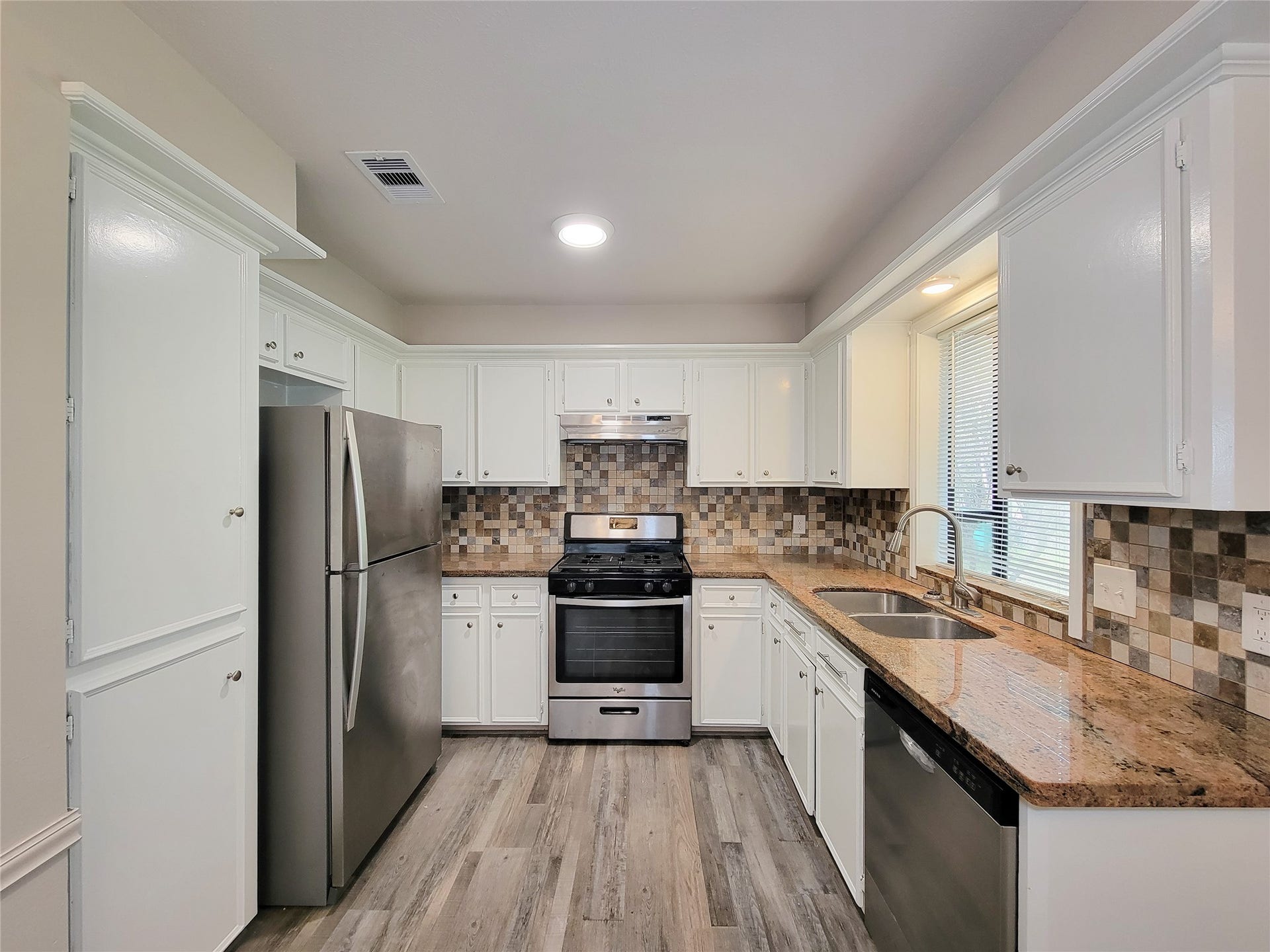80 Fallenstone Drive, The Woodlands, TX 77381 Charming kitchen with sleek stainless steel appliances, elegant granite countertops, and stylish mosaic tile backsplash, complemented by pristine white cabinetry and warm wood-look flooring.