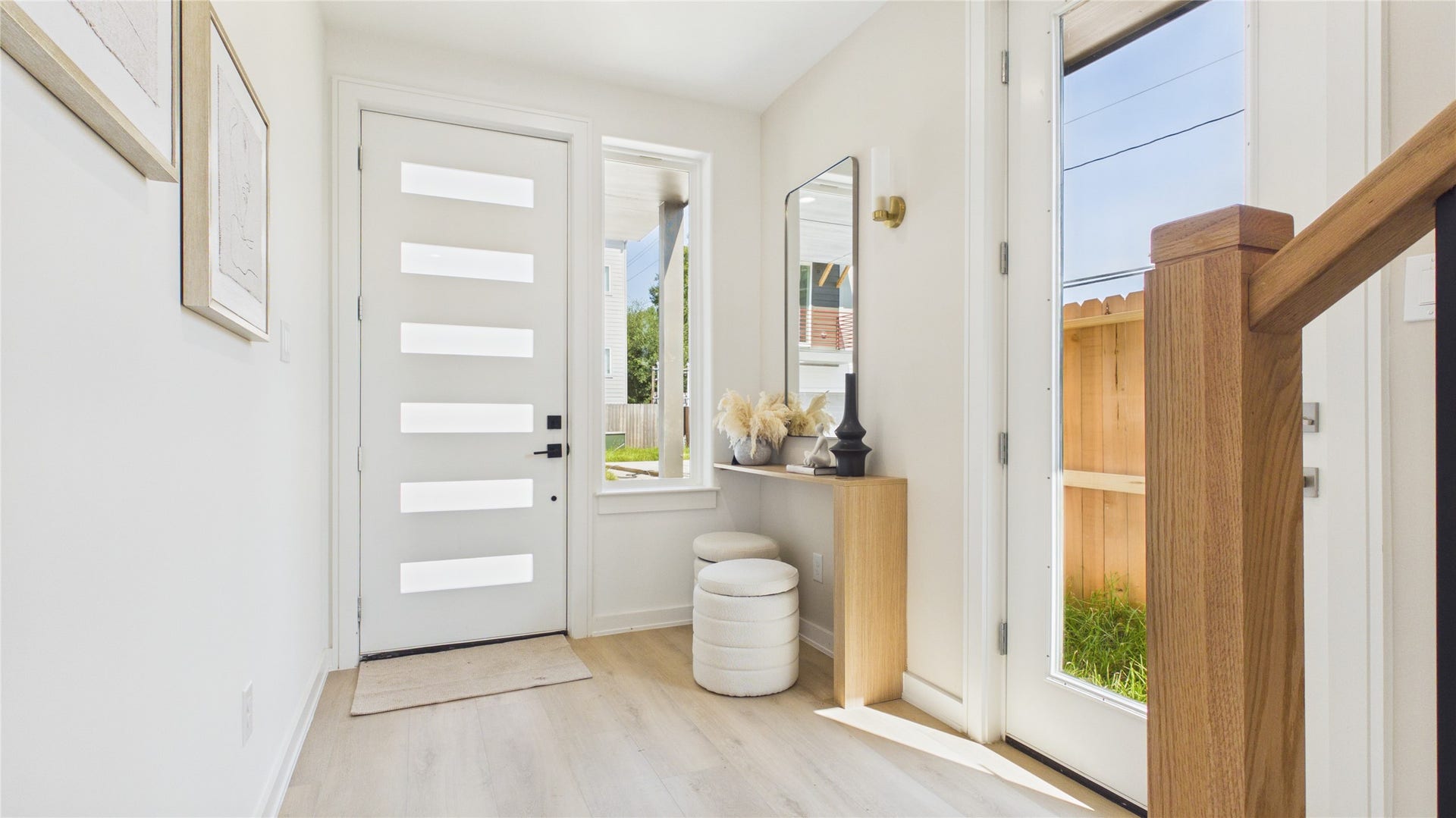 Bright and modern entryway featuring a sleek white door with frosted glass panels, light wood flooring, and a chic console with decorative accents.