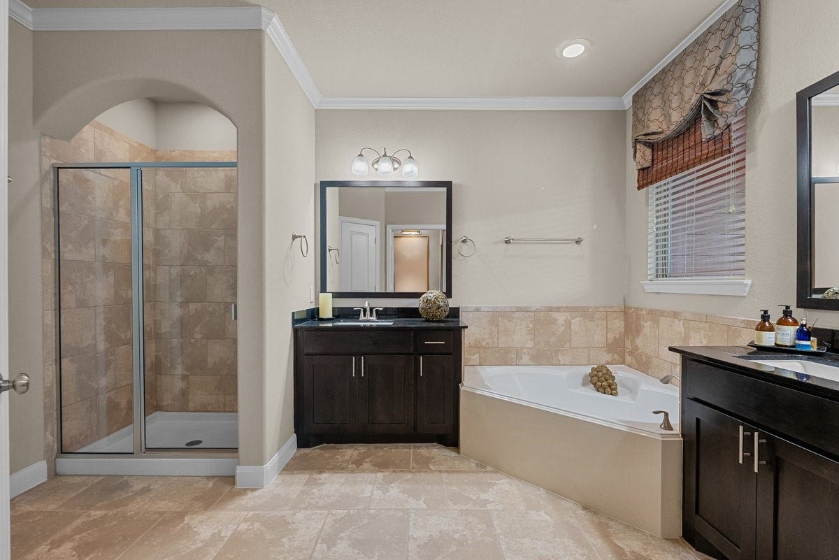 416 Via Regatta Drive, Webster, TX 77598 The spa-like primary en suite bathroom is a luxurious retreat, showcasing dual vanities with dark modern cabinetry and premium granite countertops.
