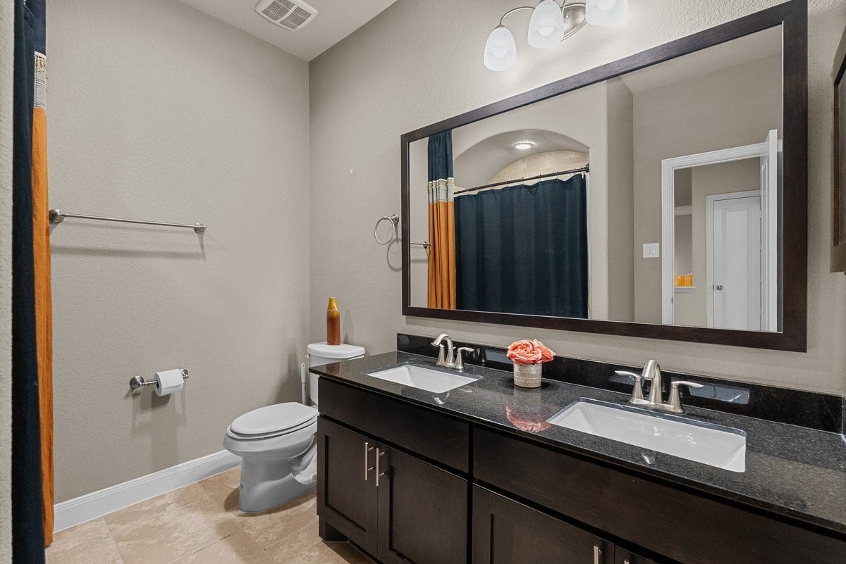 416 Via Regatta Drive, Webster, TX 77598 The spacious second-floor full bathroom is beautifully appointed, featuring a large dual vanity with rich dark cabinetry and a premium granite countertop.
An oversized, dark-framed mirror anchors the room beneath stylish updated lighting. The bathroom also includes durable tile flooring and a tub/shower combination detailed with a timeless, multi-toned tile surround.