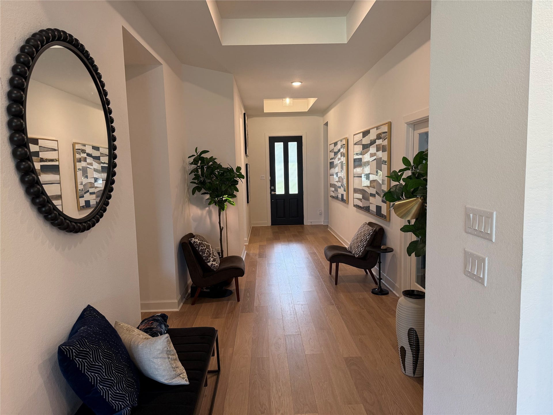 9911 Deep Water Drive, Missouri City, TX 77459 Elegant hallway with warm wood flooring, modern decor, and ample natural light leads to a striking black front door.
