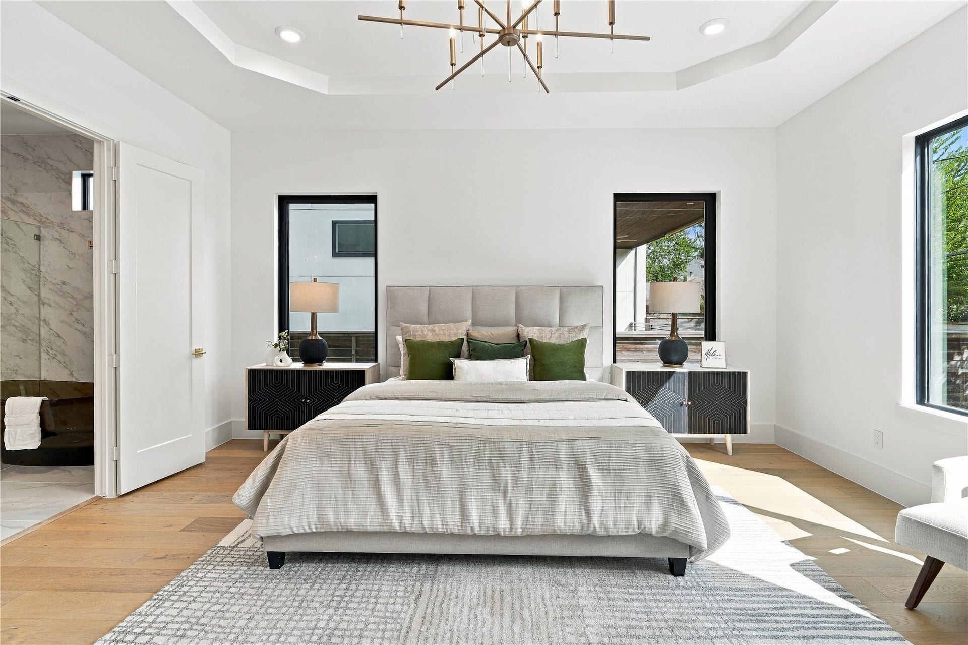 Luxurious primary bedroom featuring elegant lighting, wood flooring, and a spacious, serene layout.