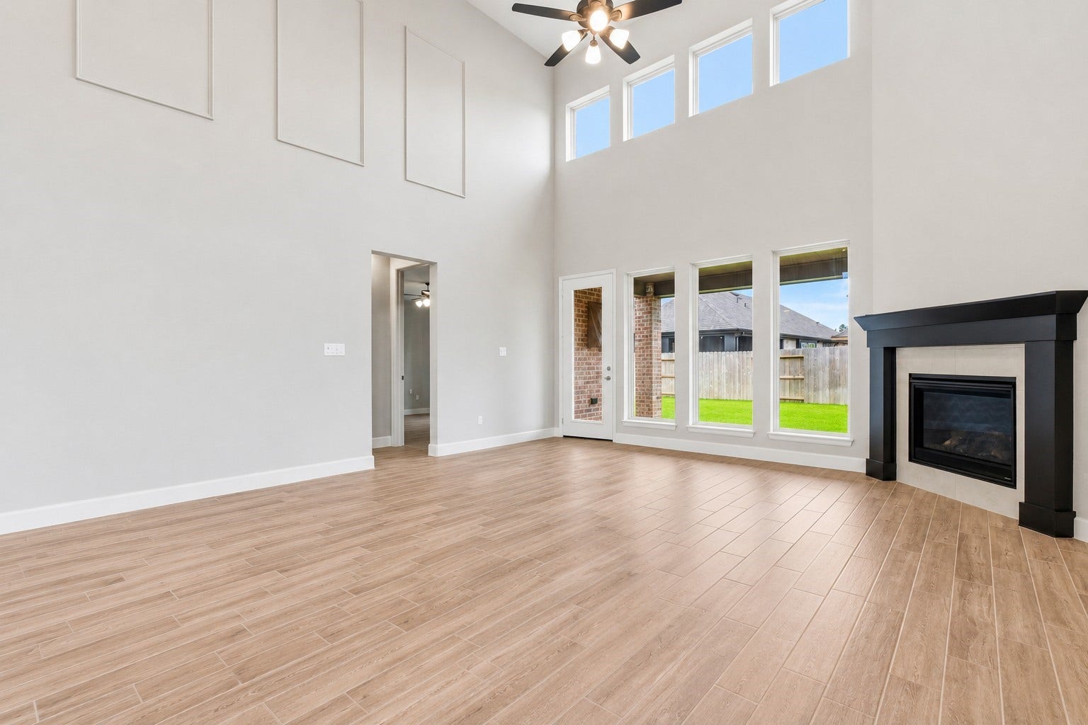 1147 Beals Creek Street, Conroe, TX 77304 The impressive living room showcases soaring 20-foot ceilings, a cozy fireplace with a beautiful wood mantel, and a dramatic wall of windows that fills the space with natural light. Primary bedroom is to the left.