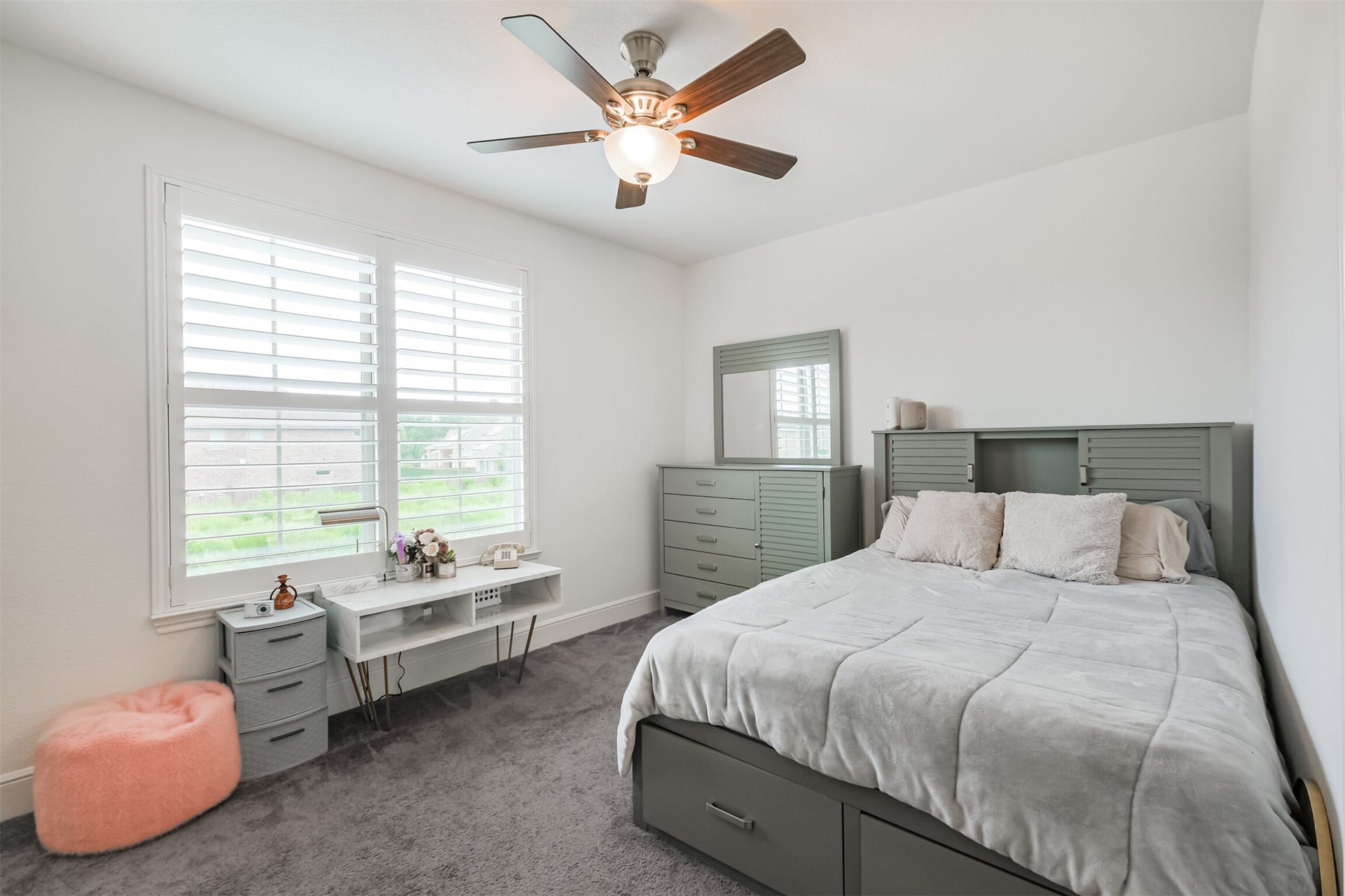 13611 Saddlebred Springs Lane, Cypress, TX 77429 Bright and inviting sixth bedroom featuring a large window with elegant plantation shutters, a ceiling fan, and a warm neutral palette with an en suite bathroom. Abundant natural light creates a serene and comfortable retreat ideal for relaxation.