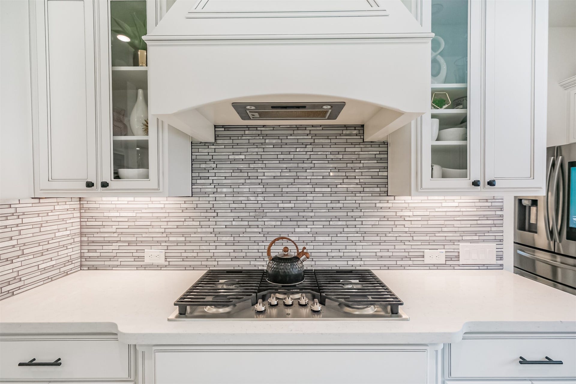 13611 Saddlebred Springs Lane, Cypress, TX 77429 Luxuriously appointed kitchen featuring custom Benedettini cabinetry with elegant glass-front display cabinets, a sleek GE gas cooktop, and a sophisticated mosaic glass backsplash.