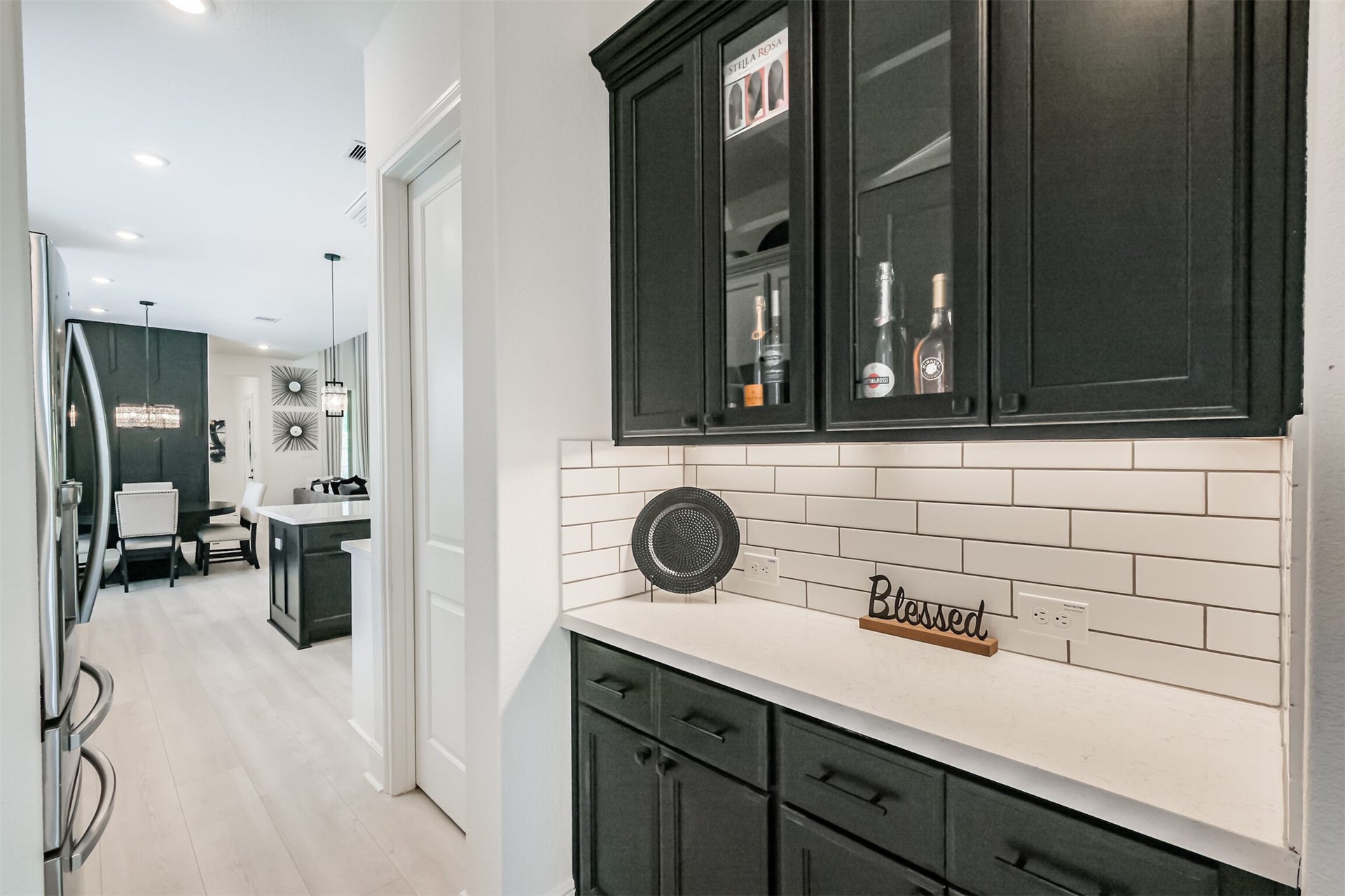 13611 Saddlebred Springs Lane, Cypress, TX 77429 Sophisticated butlers pantry featuring sleek black cabinetry with elegant glass-front accents, a crisp white subway tile backsplash, and undercabinet lightingcreating a polished and functional space ideal for entertaining and additional storage.