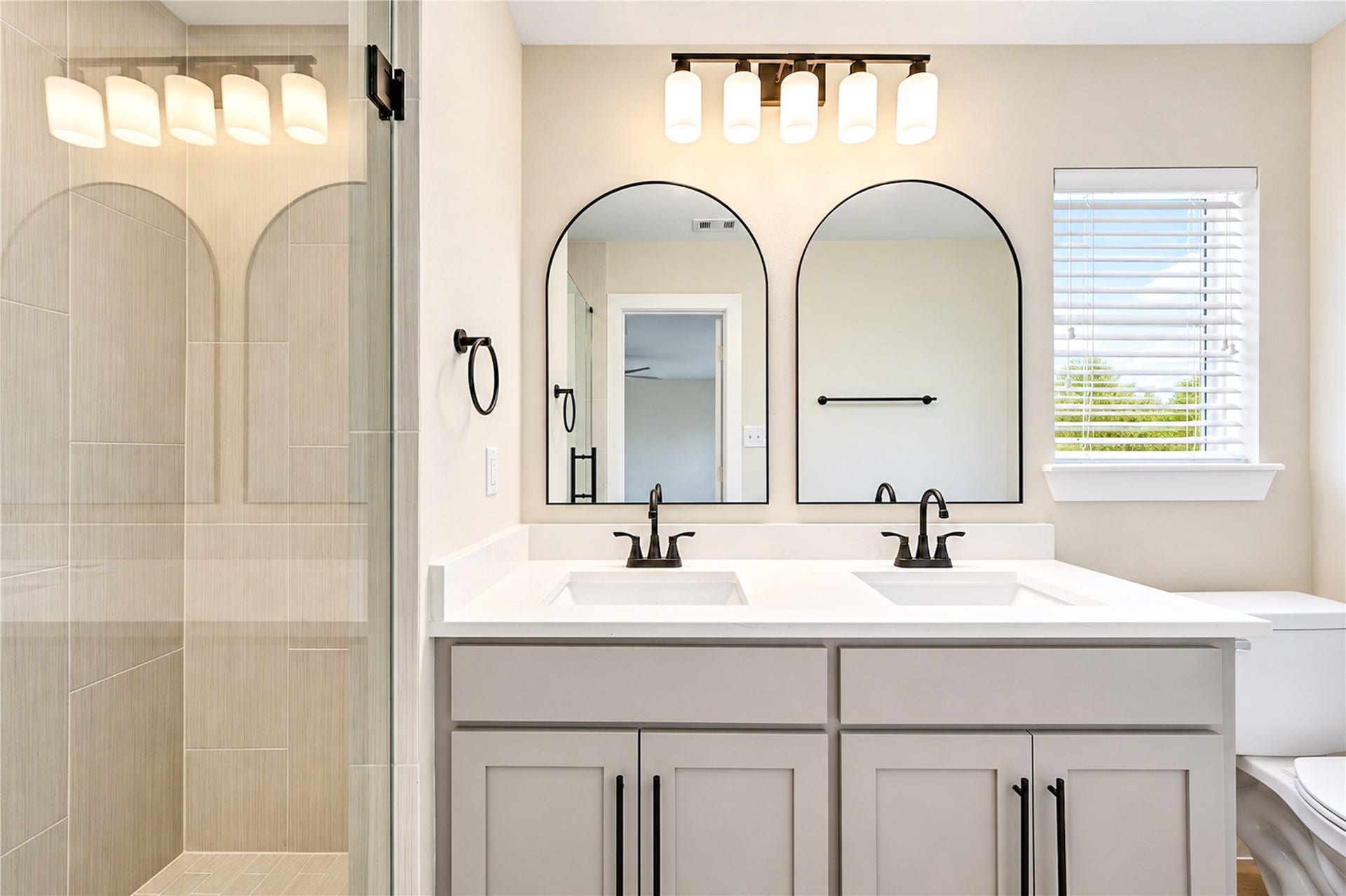 10607 Del Monte Drive, Houston, TX 77042 Beautifully remodeled primary bathroom features a dual-sink vanity with elegant Shaker-style cabinetry, soft-close doors, new faucets, arched mirrors, designer lighting, and stylish contemporary finishes.