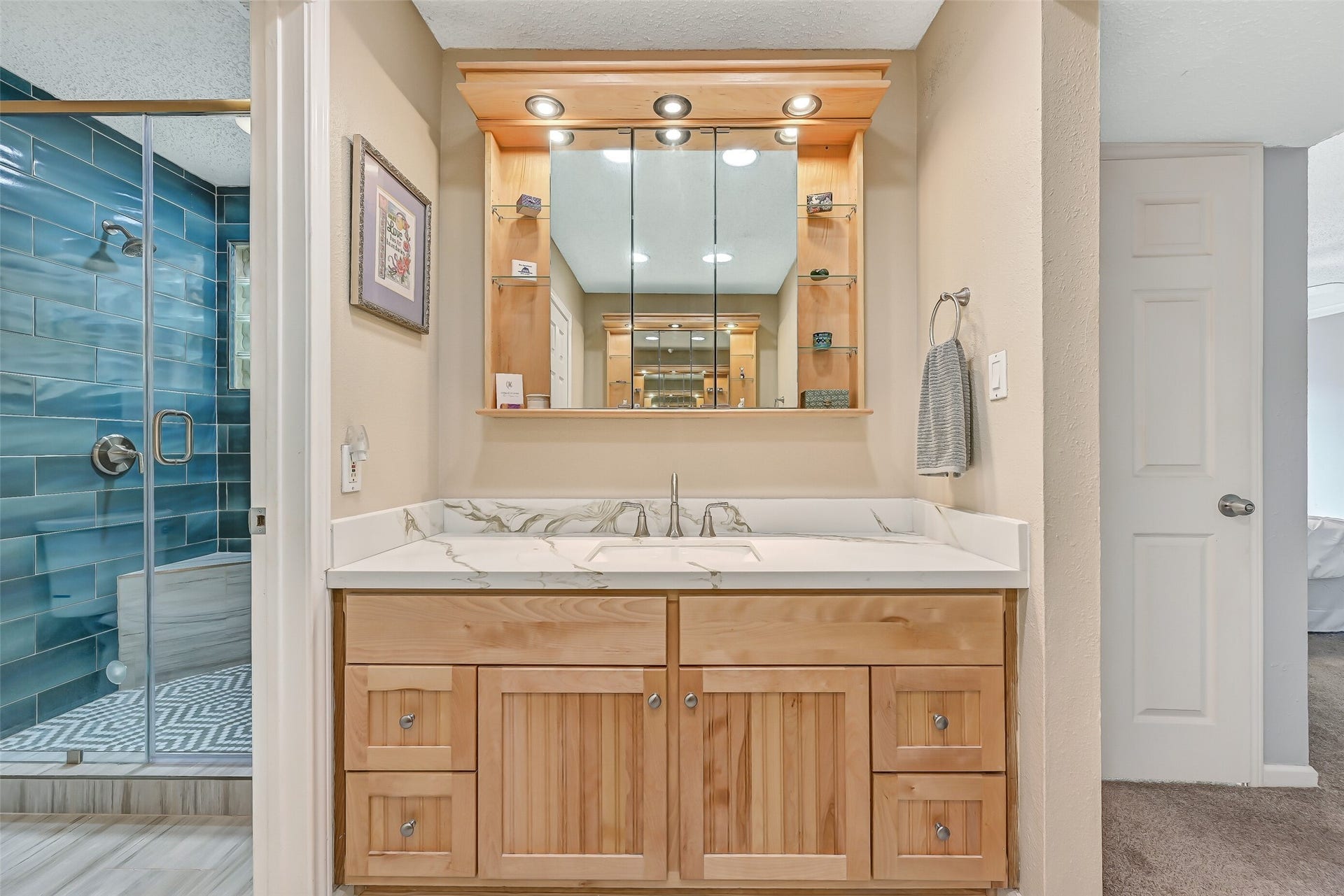 18214 Bal Harbour Drive, Nassau Bay, TX 77058 The second vanity continues the primary bath's coordinated finishes with quartz countertops, an oak-finish cabinet, porcelain sink & brushed-nickel fixtures. Above, a custom mirrored storage cabinet features illuminated glass shelving and additional concealed storage, while the remodeled shower is visible just beyond.