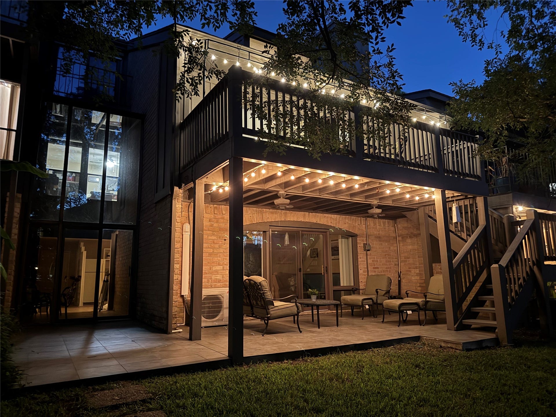 18214 Bal Harbour Drive, Nassau Bay, TX 77058 Enjoy the beauty of waterfront living as the sun sets! The rear of this private townhome shines in the evening glow, showcasing a two-story glass-enclosed sunroom, spacious ground-level patio, and extended Trex-decked composite balcony above, accented by warm string lighting.