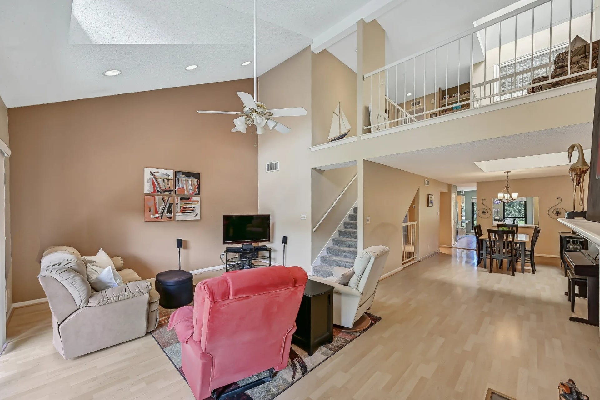 18214 Bal Harbour Drive, Nassau Bay, TX 77058 Looking back across the living room reveals the open connection to the separate dining area and kitchen, with light laminate flooring extending throughout. The third-floor loft overlooks the main living spaces, while a carpeted staircase provides access to the private primary suite above.