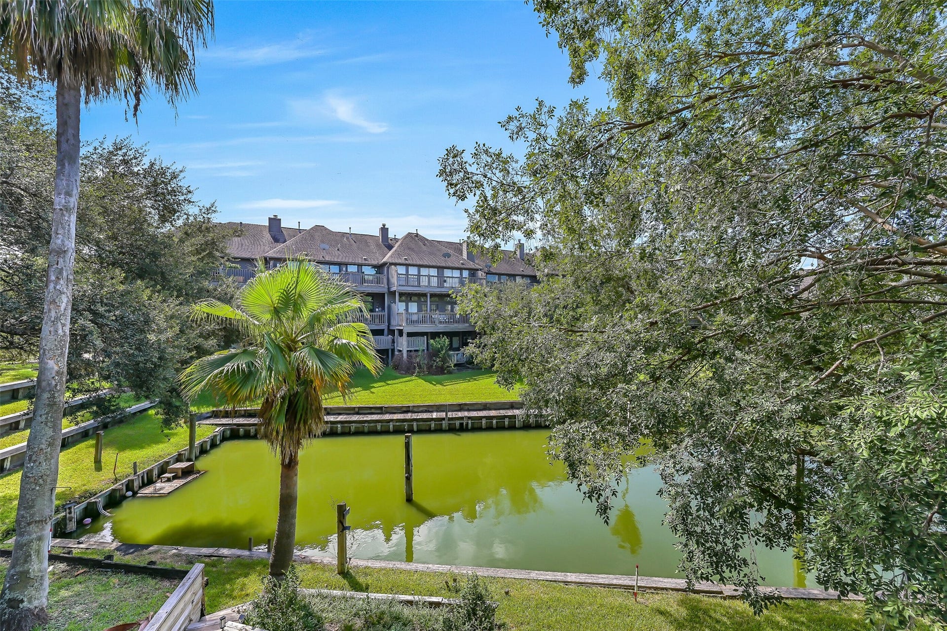 18214 Bal Harbour Drive, Nassau Bay, TX 77058 A view from the second-floor balcony reveals the canal below, framed by mature trees and neighboring waterfront townhomes. The property's included 39' boat slip with electricity is located directly behind the home, offering convenient boating access to Clear Lake, Galveston Bay & beyond.