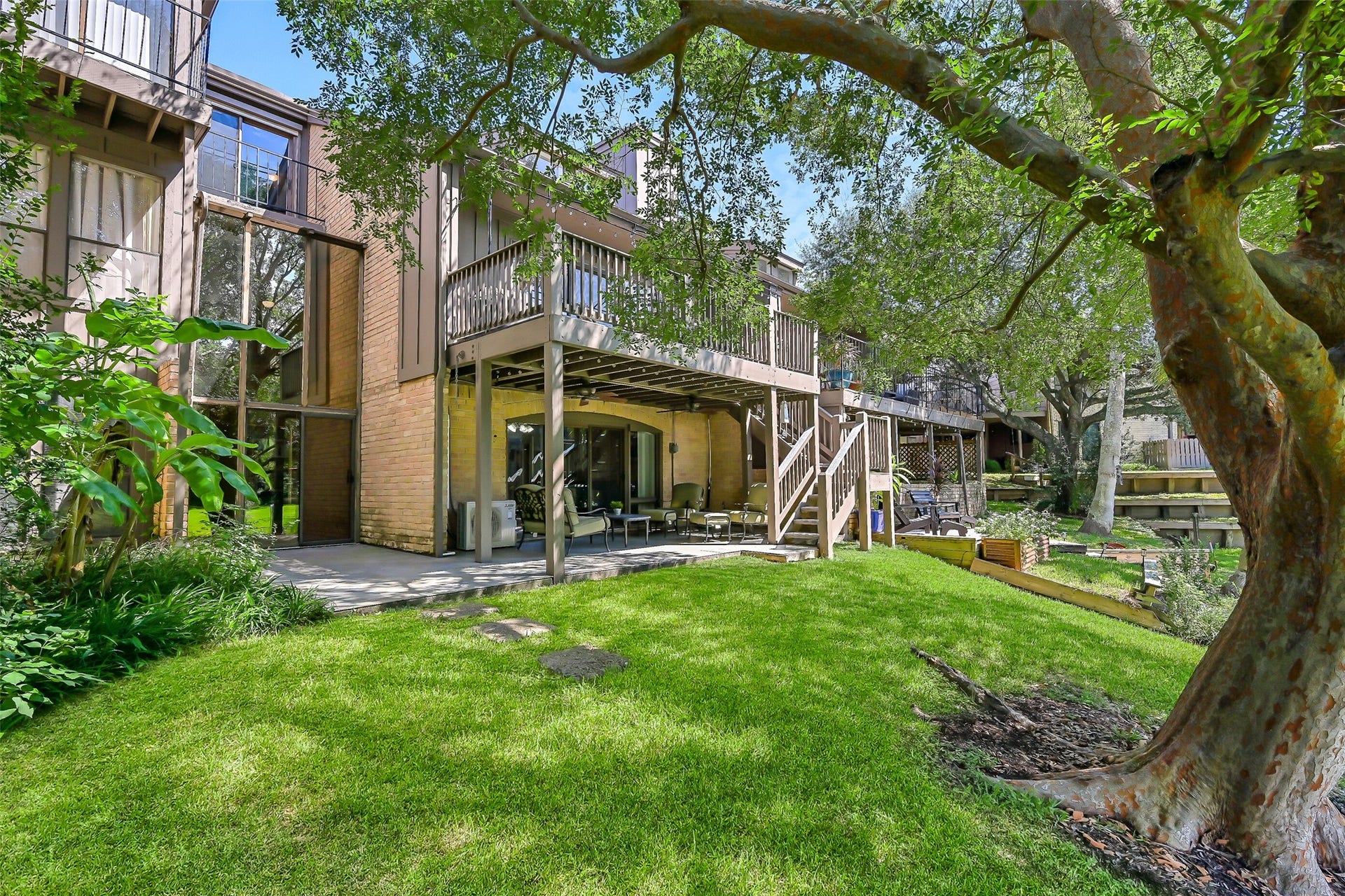 18214 Bal Harbour Drive, Nassau Bay, TX 77058 The rear of this private townhome showcases its two-story glass-enclosed sunroom, spacious ground-level patio & extended composite balcony above. Exterior stairs connect the two outdoor living areas, while the mature Chinese Elm, grassy waterfront setting & canal just steps away complete the picture.