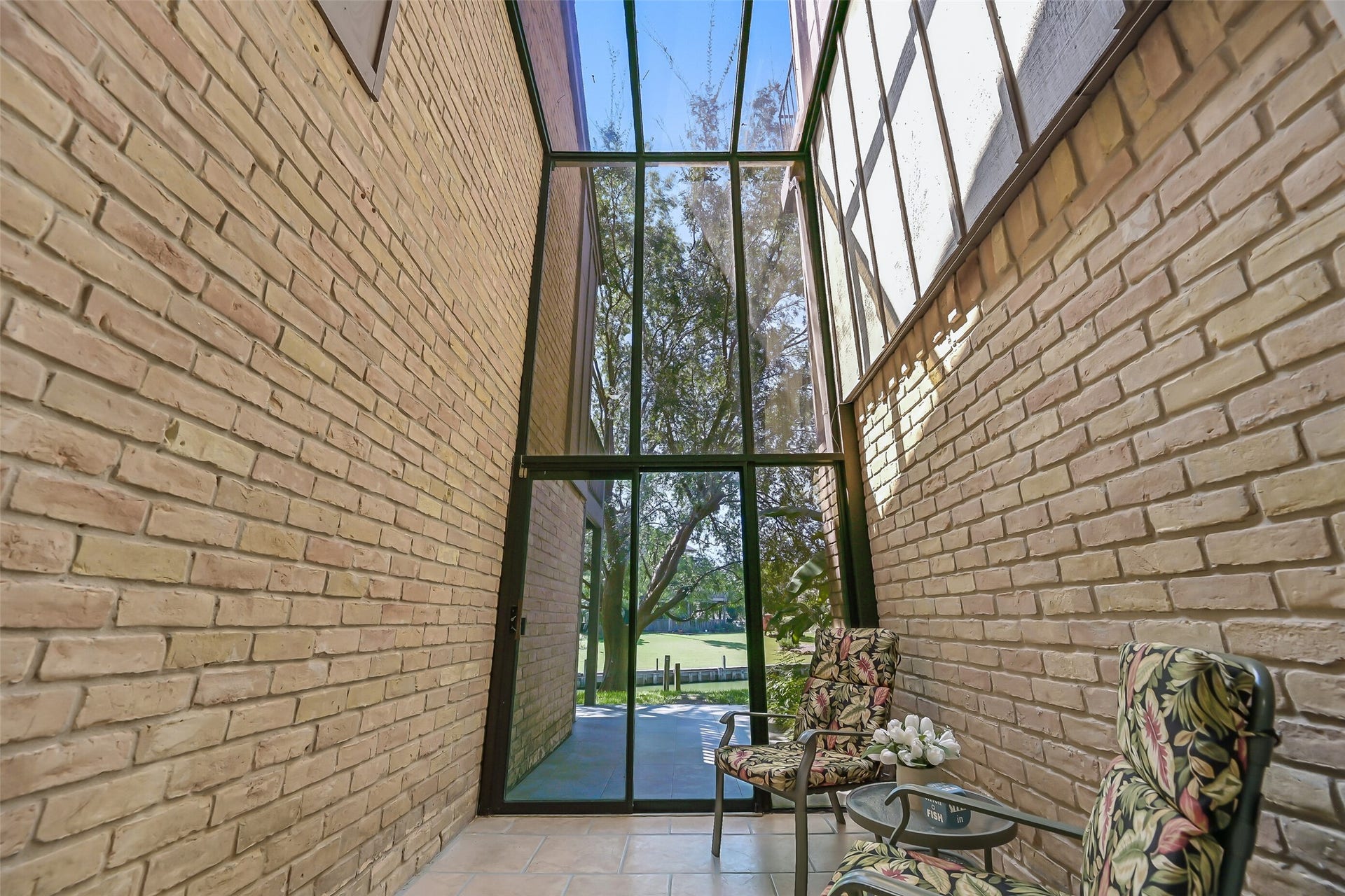 18214 Bal Harbour Drive, Nassau Bay, TX 77058 A truly unique feature, the two-story sunroom is framed by soaring brick walls and floor-to-ceiling glass overlooking the canal and mature elm. A sliding glass door opens to a 15' x 8' tiled patio, while the enclosed space offers possibilities for a sitting area, dining space or additional flex use.