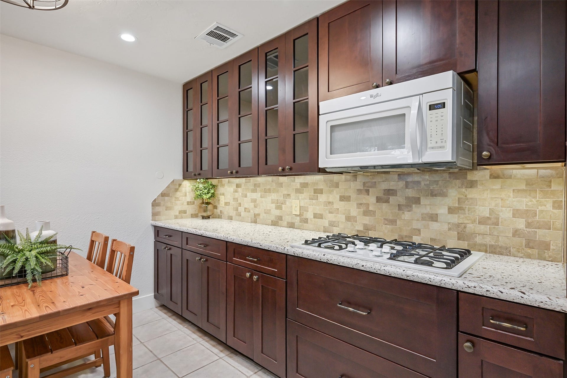 5403 Carmona Lane, Pearland, TX 77584 Thoughtful details include a 5-burner gas cooktop, built-in microwave, granite counters & subway-style travertine backsplash illuminated by under-cabinet lighting. Glass-front upper cabinets add display space, while deep pots & pans drawers and abundant lower cabinetry keep cookware close at hand.