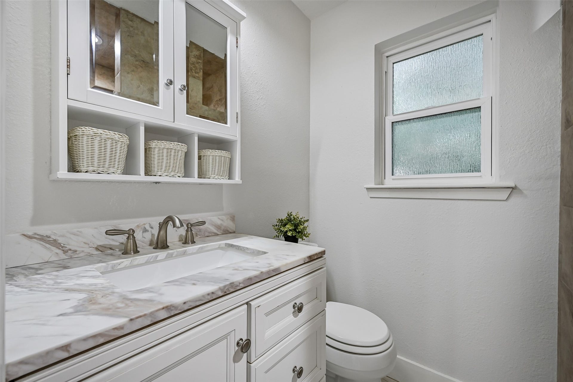 5403 Carmona Lane, Pearland, TX 77584 The updated en suite bath pairs a crisp white vanity with marble countertop, rectangular undermount sink & built-in mirrored storage above. A privacy-glass window brings in natural light, while the oversized tiled walk-in shower sits just beyond the vanity.