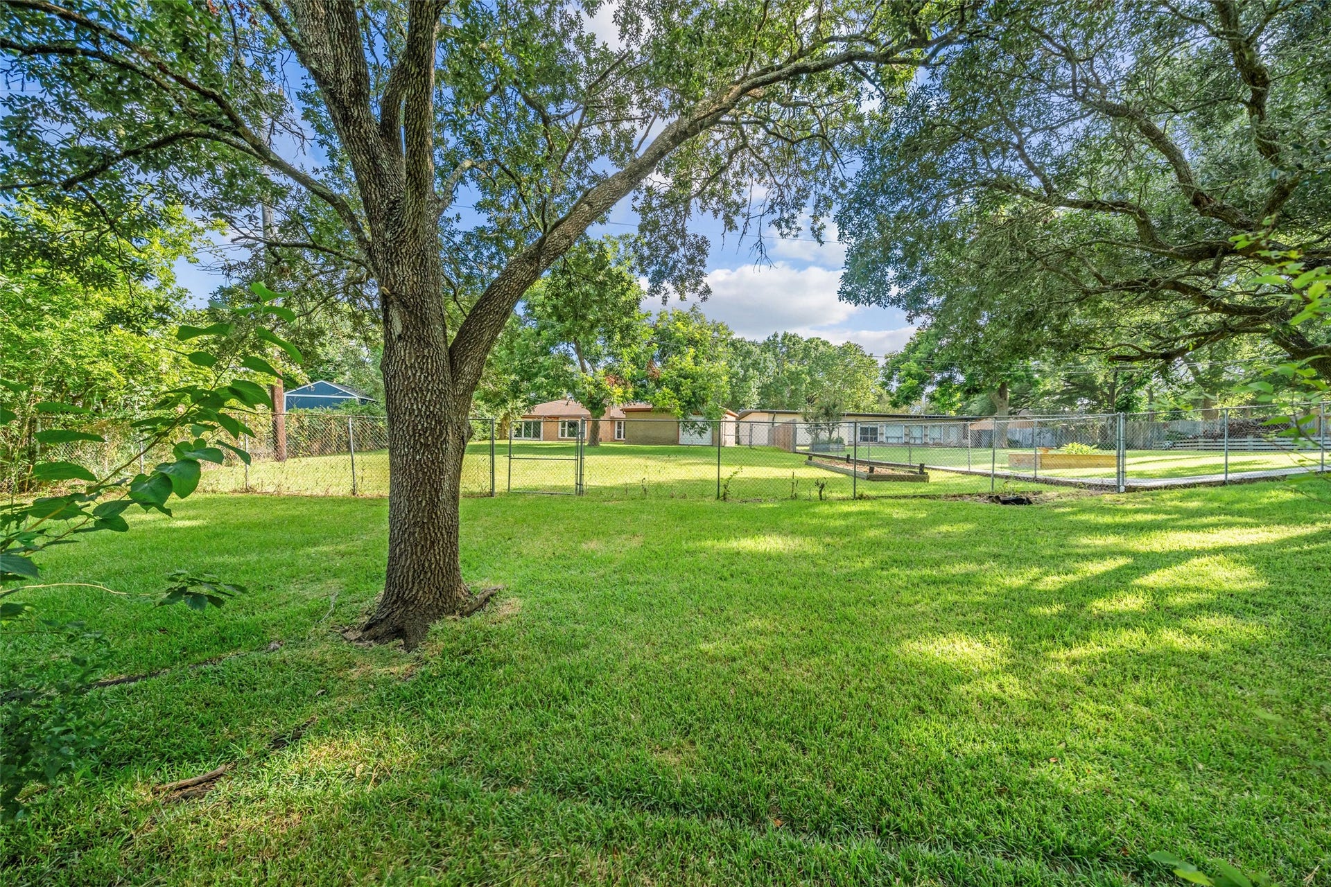 7714 Pecanwood Street, Hitchcock, TX 77563 A great view of the home and property from boat dock. Yard is fully fenced and ready for your pets! In the right of the photo within the fence is a garden.