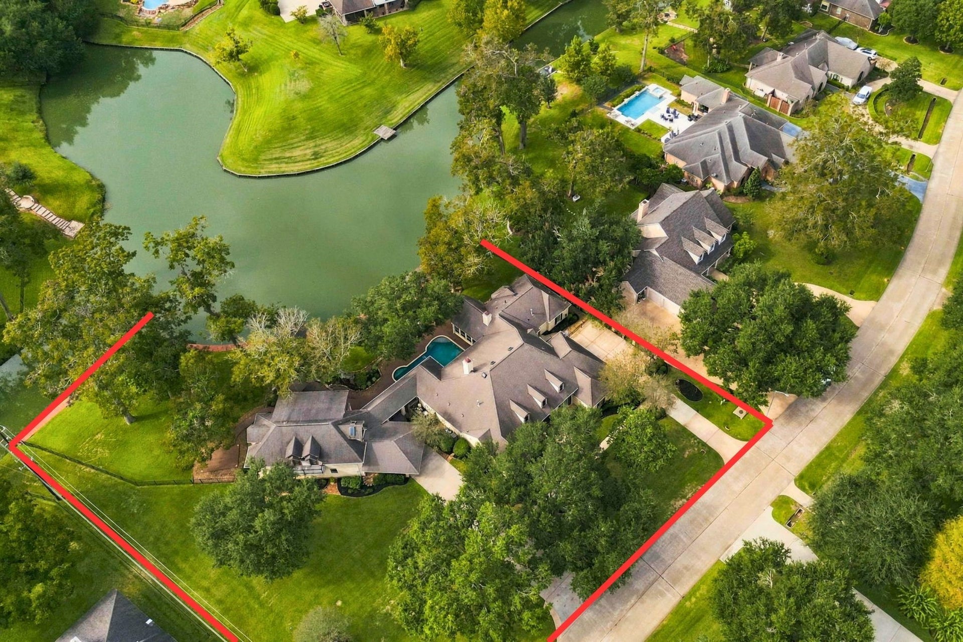 4711 Westerdale Drive, Fulshear, TX 77441 This aerial view captures the magnificent scale of the property and its beautiful waterfront setting, showcasing the expansive grounds, mature trees, and surrounding landscape. Property lines outlined in red are approximate and provided for illustrative purposes only.