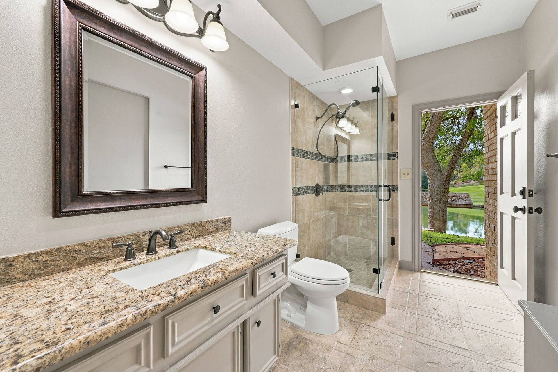 4711 Westerdale Drive, Fulshear, TX 77441 The main home offers three Full Bathrooms, including this conveniently located Full Bath with direct access to the backyard, making it ideal for use as a pool bath. Features include light cabinetry, granite countertops, an undermount sink, a framed mirror, and an oil-rubbed bronze widespread faucet. A walk-in shower with a frameless glass enclosure completes this well-appointed space.