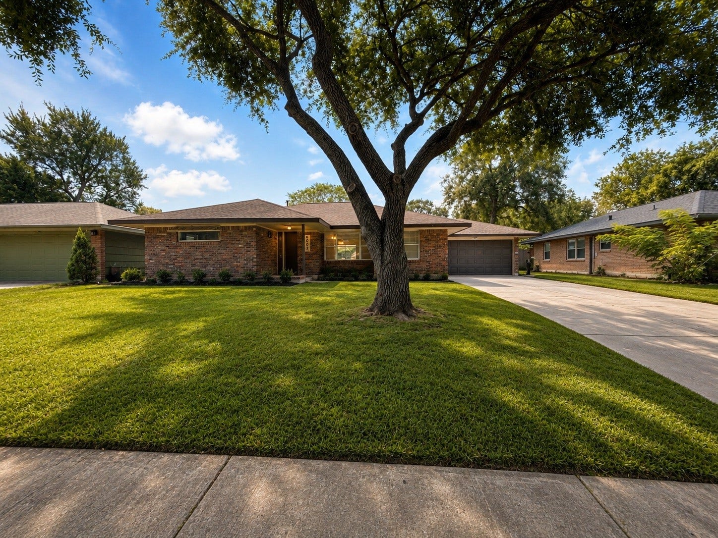 Single-story brick home with a mature shade tree, wide driveway and attached two-car garage.