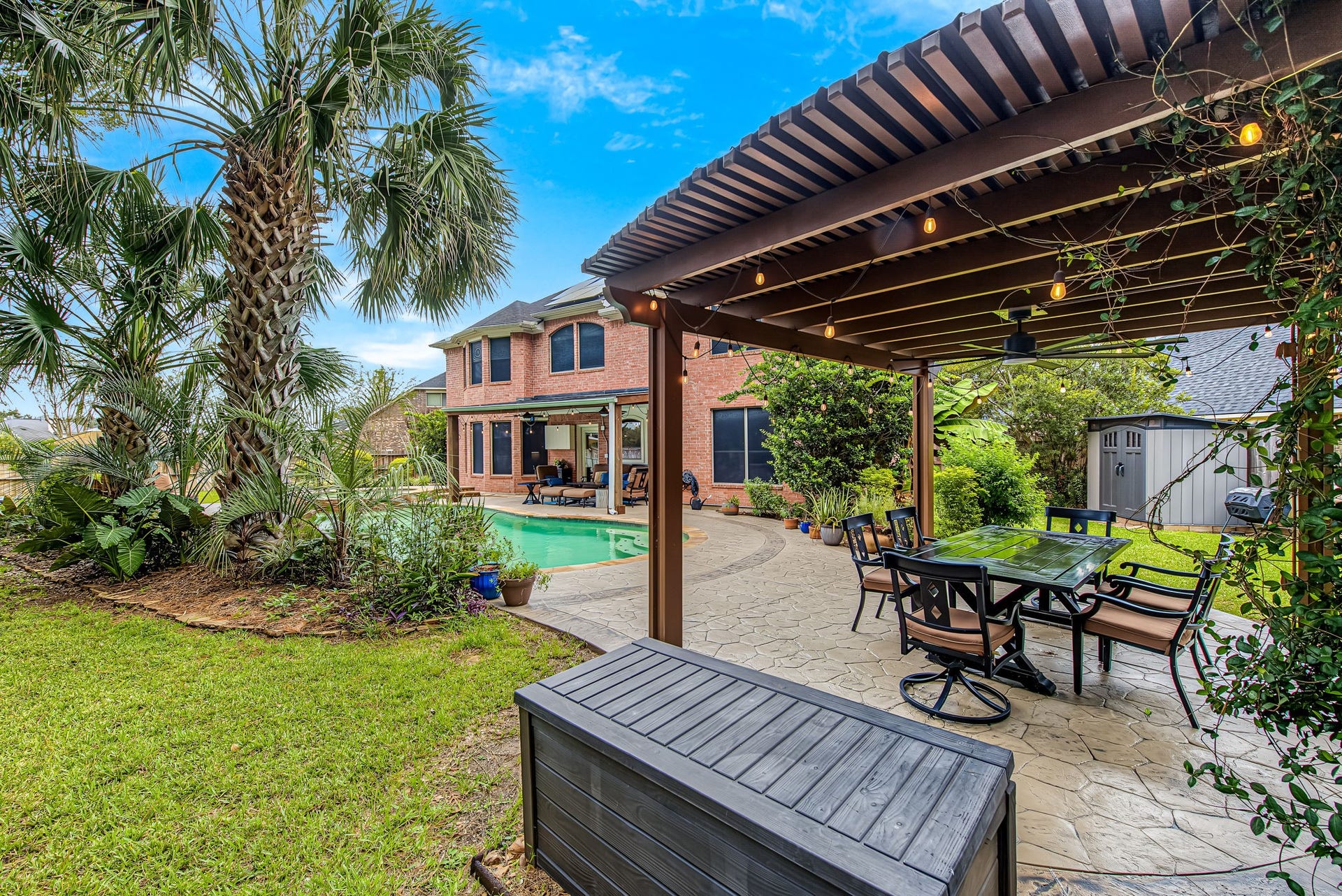 21223 Dover Park Lane, Katy, TX 77450 Experience outdoor living at its finest with a spacious patio featuring a pergola, dining area, and a sparkling pool, all set against a backdrop of lush greenery and a charming brick home.