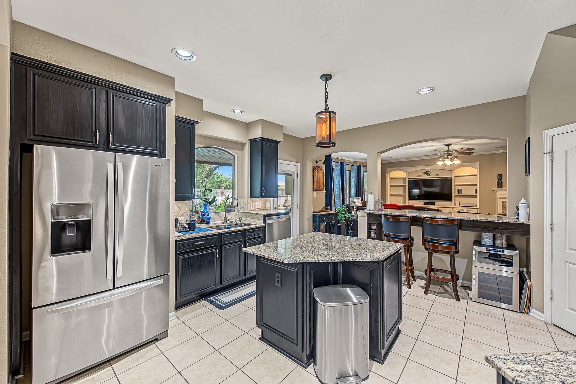 21223 Dover Park Lane, Katy, TX 77450 Modern kitchen featuring sleek stainless steel appliances, elegant dark cabinetry, and a central island with granite countertops, seamlessly connected to the inviting living area with a breakfast bar.