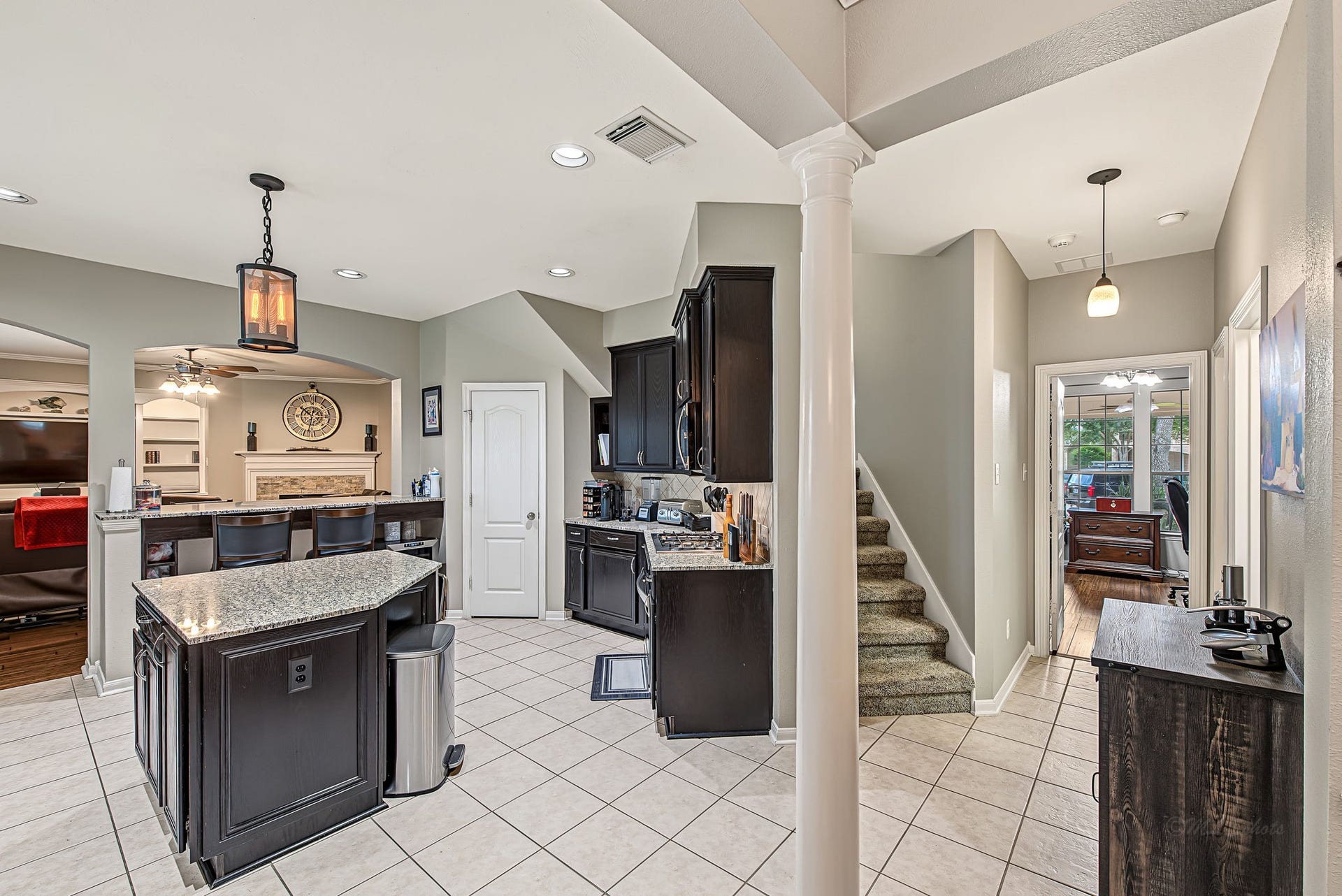 21223 Dover Park Lane, Katy, TX 77450 Bright and inviting kitchen with elegant dark cabinetry, granite countertops, and a convenient breakfast bar overlooking the cozy living area. A stylish staircase leads to the upper level, while a well-lit hallway offers easy access to additional rooms.