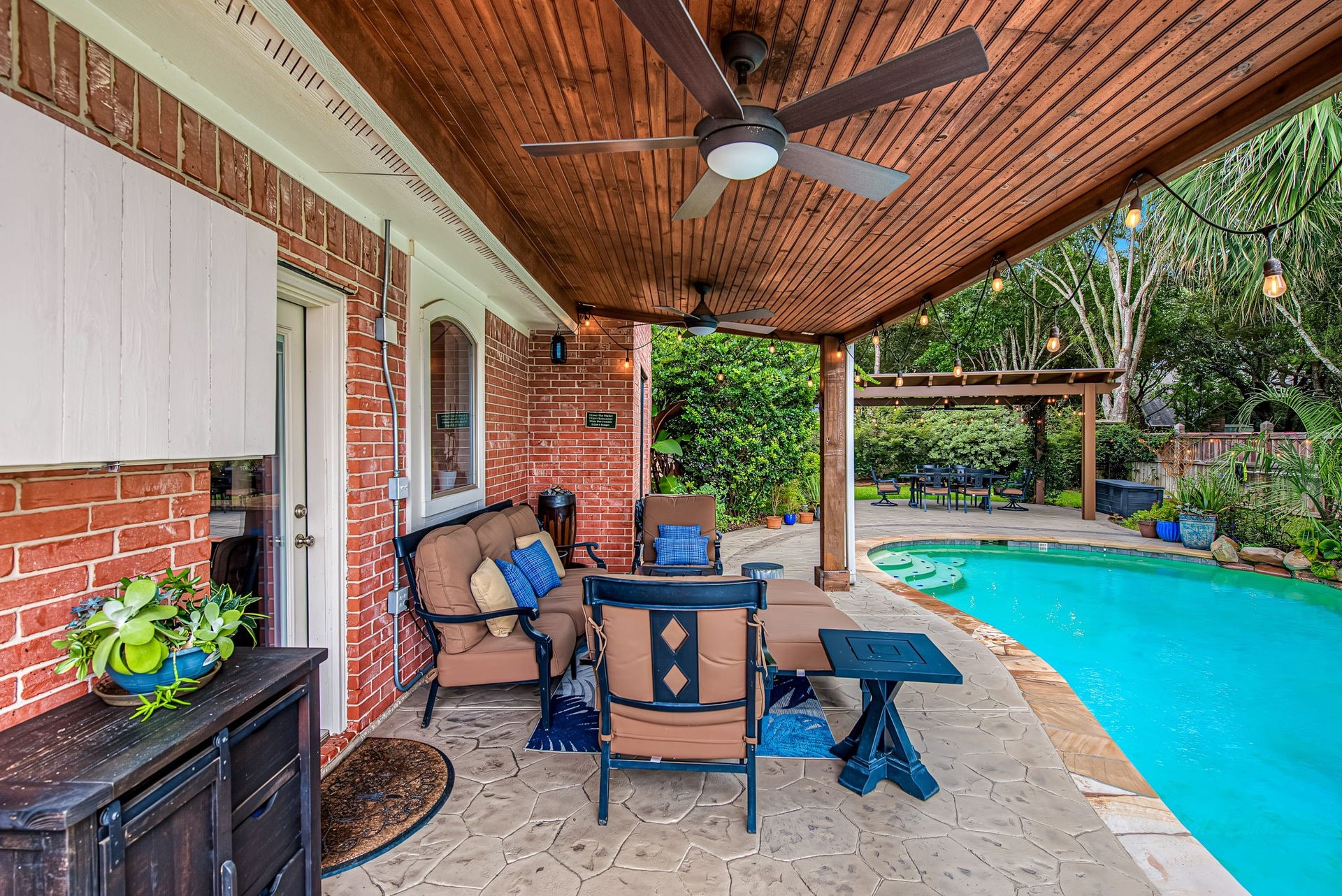 21223 Dover Park Lane, Katy, TX 77450 Charming covered patio with a ceiling fan overlooks a sparkling pool, surrounded by lush greenery and a cozy seating area perfect for outdoor relaxation and entertaining.